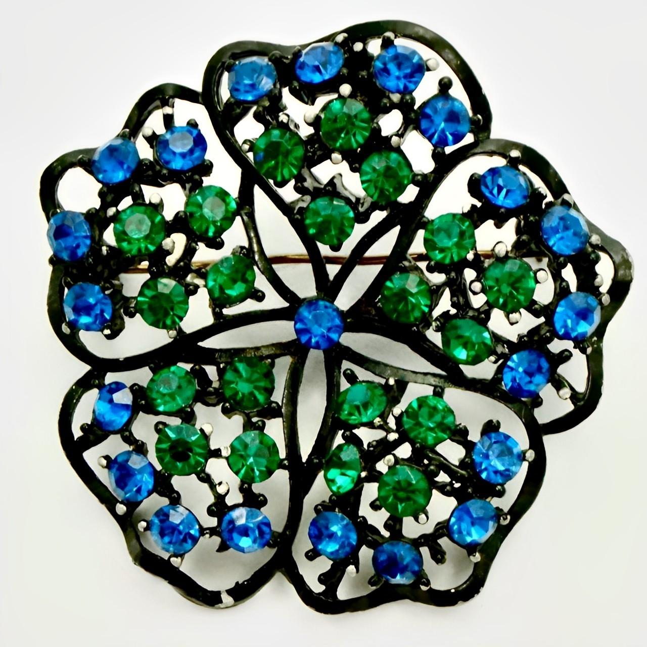 Japanned electric blue and emerald green crystal flower brooch and leaf clip on earrings. The brooch measures diameter 5 cm / 1.9 inches. The earrings are 3.1 cm / 1.2 inch by 1.9 cm / .7 inch. There is wear to the black japanned finish. The brooch