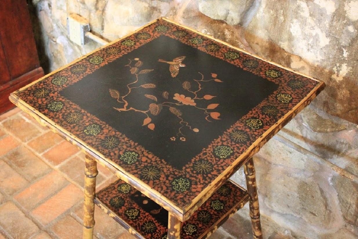 Edwardian bamboo table with lower shelf. Bamboo painted with faux tortoise technique. Table top and shelf painted with center floral and bird scenes encircled by painted borders punctuated with unique circular images.