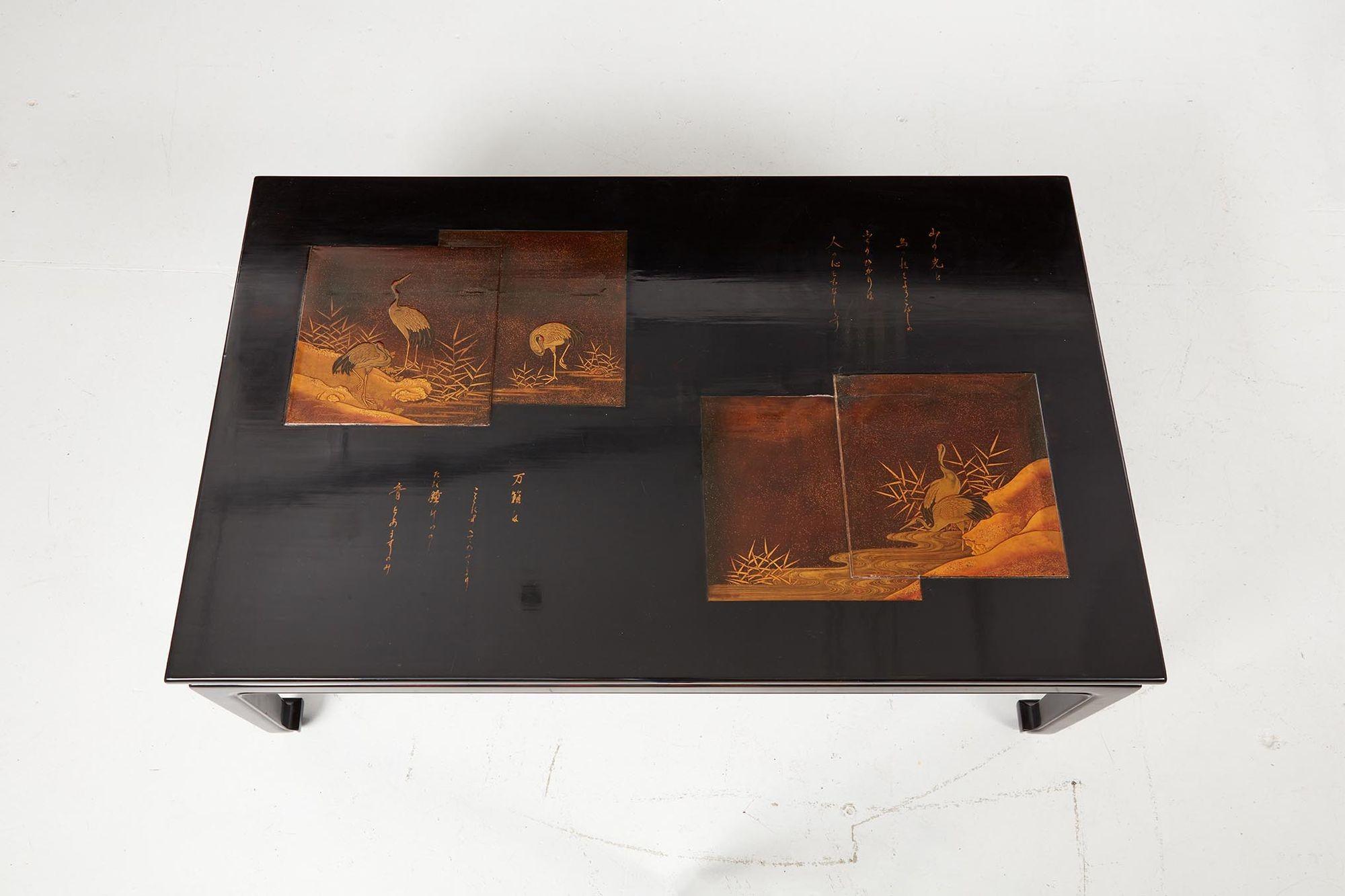 A sleek black lacquer coffee table with Japanese lakeside scenes of cranes and bamboo in gold, with two sections of Japanese script, the inset panels mounted on a rectangular top over a base with a deep concave edge apron and standing on square