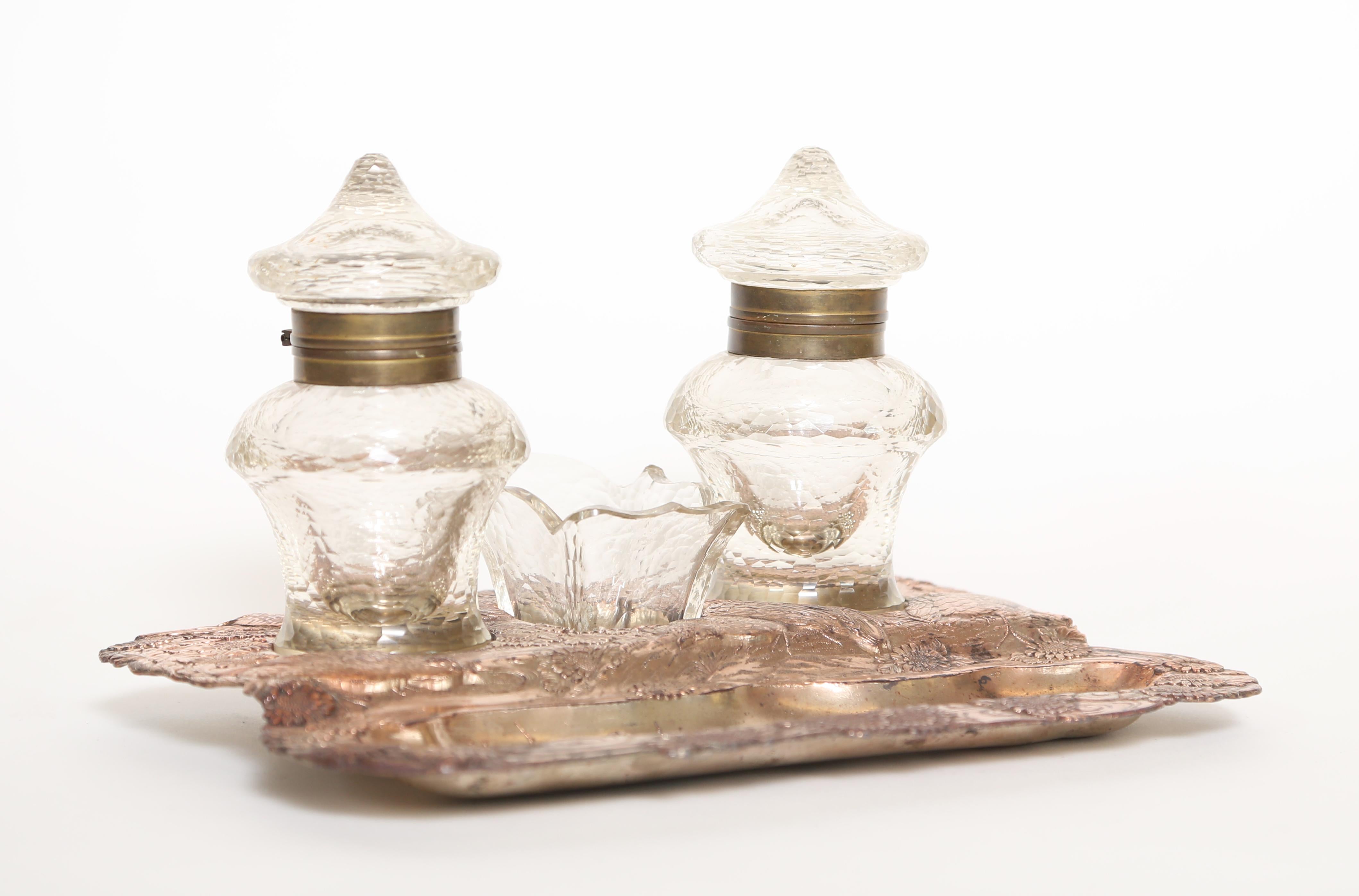 Antique coppered Japonais Revival inkstand with two ink pots and a stamp holder. The border of the base is in relief and abounds with flowers and birds while the pen rest has a quaint village scene. The glass pieces are blown and cut to resemble the