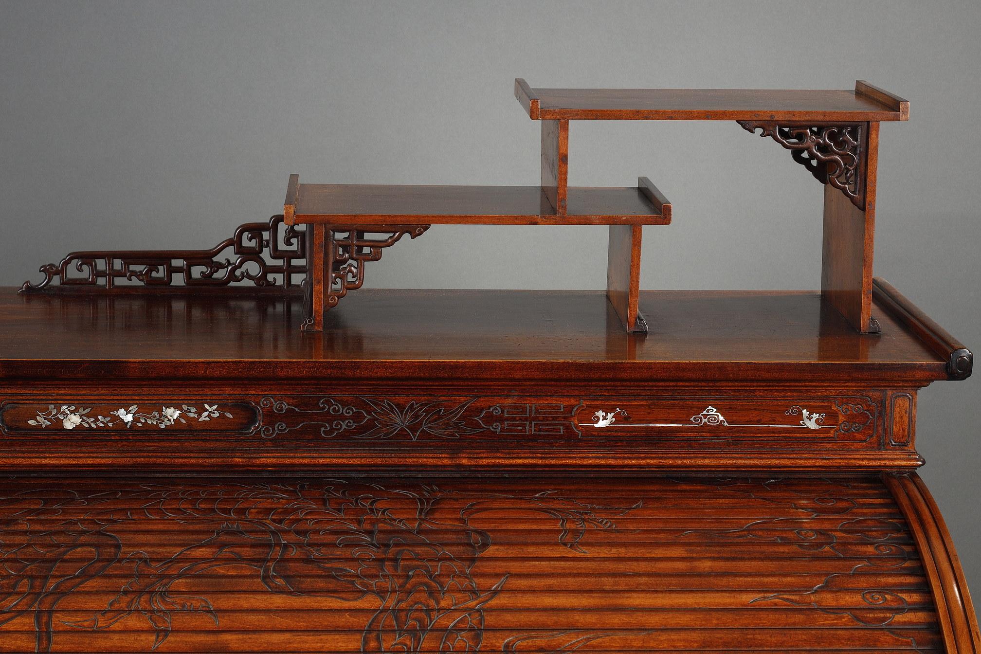 Rare bureau à cylindre de style japonais en bois teinté et sculpté, richement gravé sur toutes les faces de feuillages, de branches de cerisier et d'entrelacs géométriques. Surmonté de deux étagères asymétriques, le cylindre est décoré d'un dragon