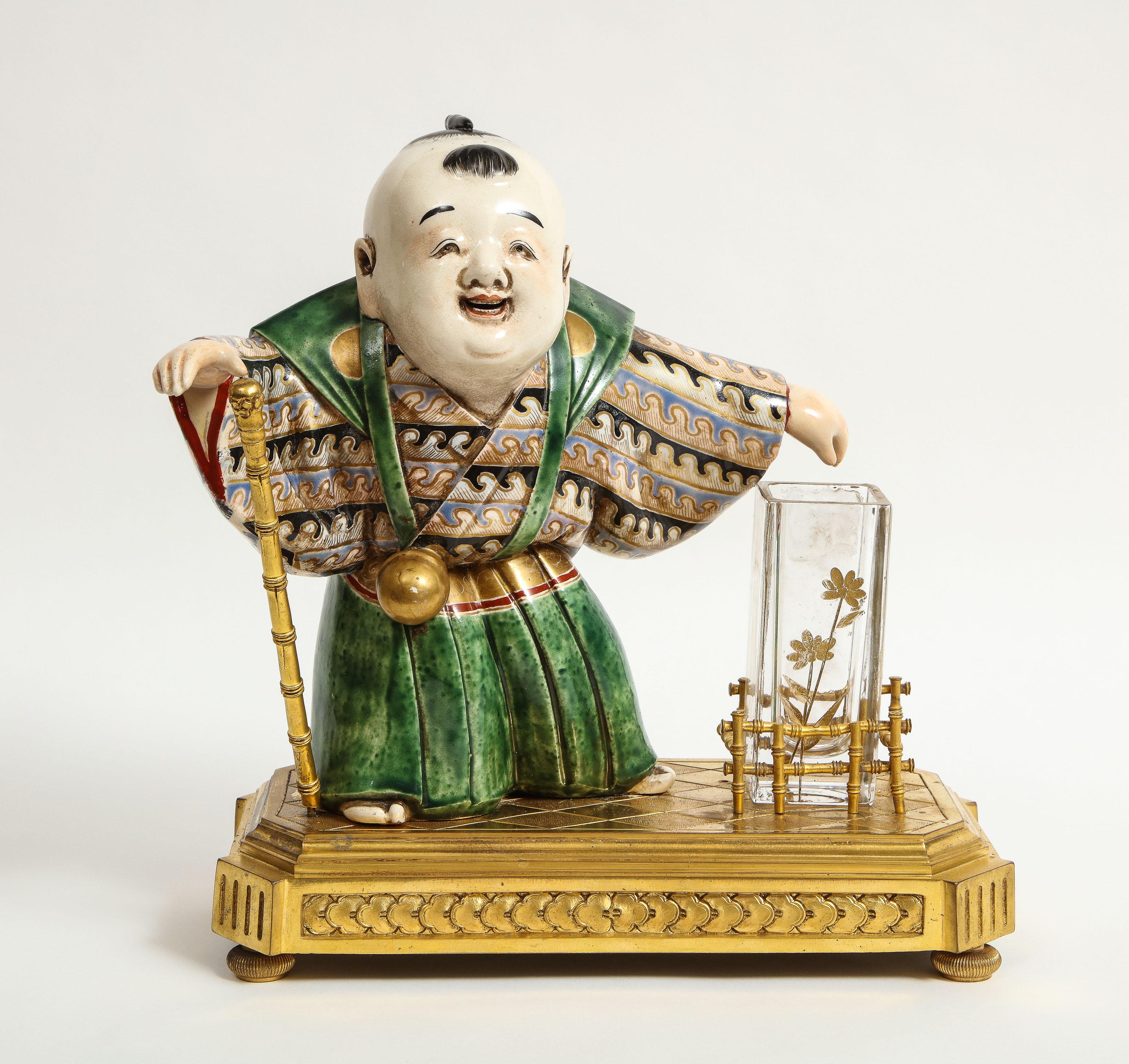 Japonisme French Ormolu, Japanese porcelain and glass centerpiece, circa 1870. Attributed to L' Escalier de cristal, Paris.

Depicting a Japanese porcelain boy, holding a bronze staff in his hand, with a glass flower vase inserted in a bronze bamboo