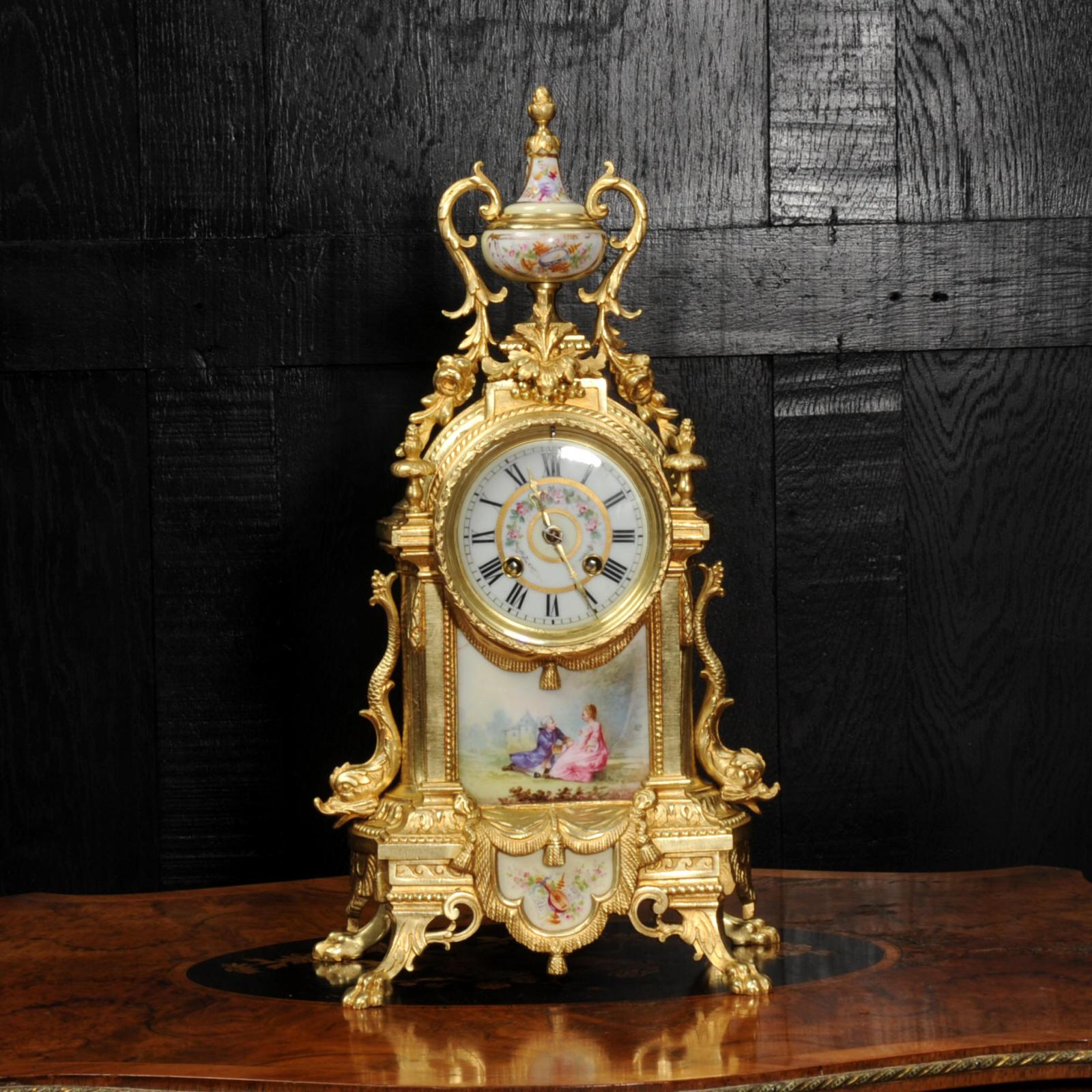 A beautiful antique French gilt bronze clock, mounted with exquisite Sèvres porcelain and with movement by Japy Frères. The large panel shows a gentleman proposing to a lady in a tranquil country setting, a chateau in the background. It is Louis XVI