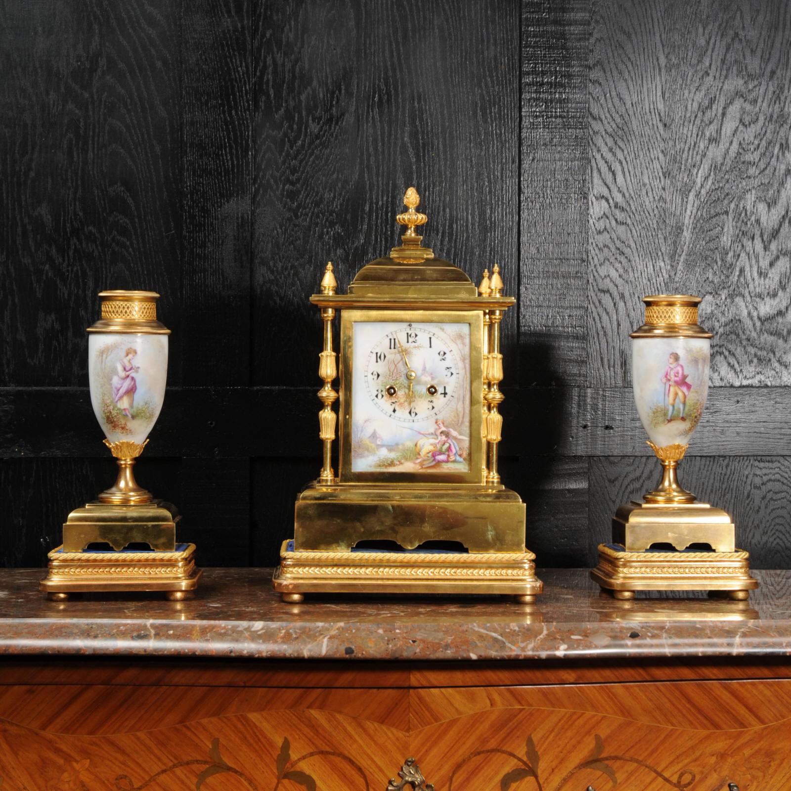 A beautiful classical clock set, of excellent quality in ormolu (finely gilded bronze) and delicately painted porcelain. The dial is finely painted with a scene of a young couple seated by a river in a country setting. The side urns also show the