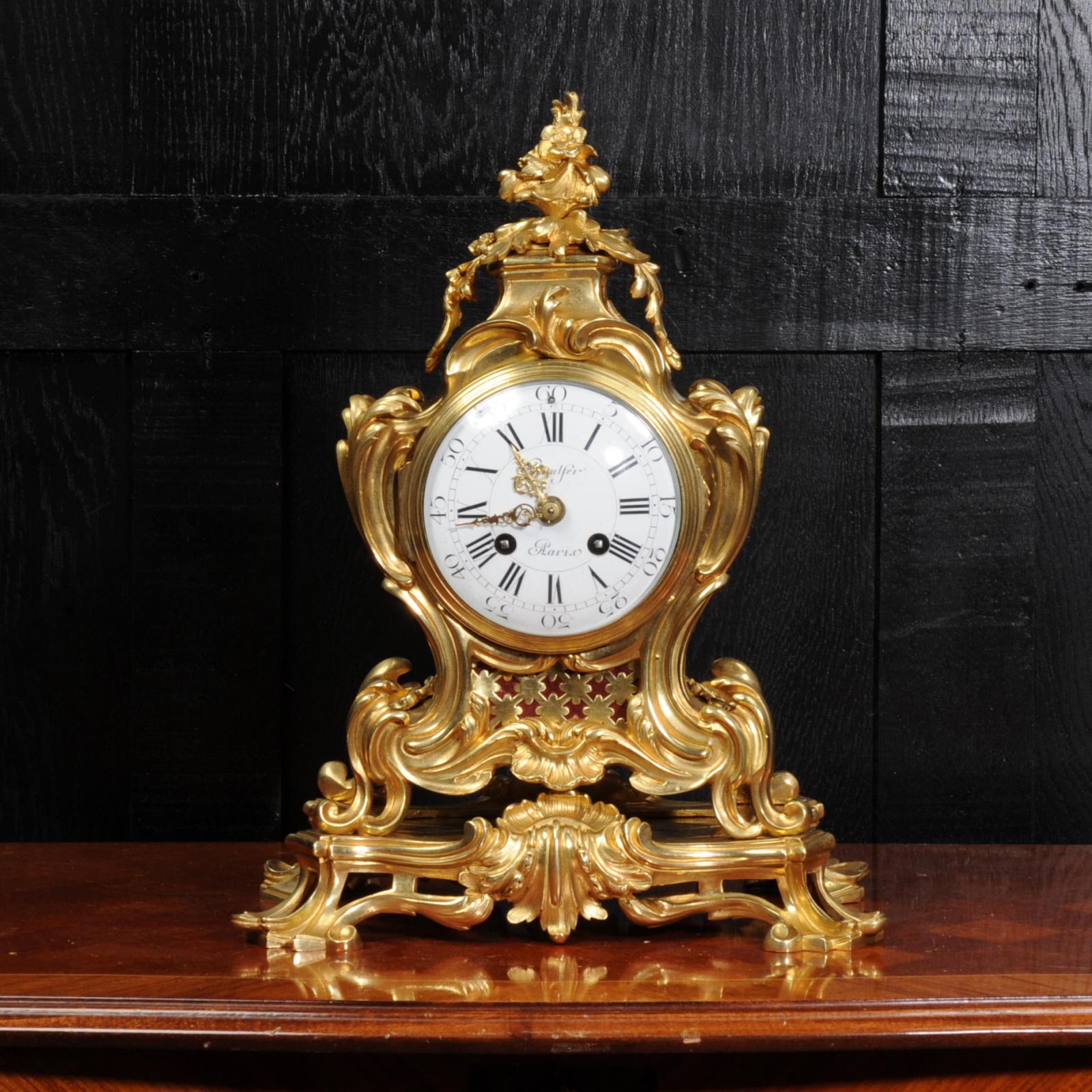 A stunning original antique French Rococo clock, circa 1870. It is beautifully sculptured with finely finished scrolls, curves and acanthus leaves in finely gilded bronze. Panels backed with red fabric lighten the design and the rear door is glazed
