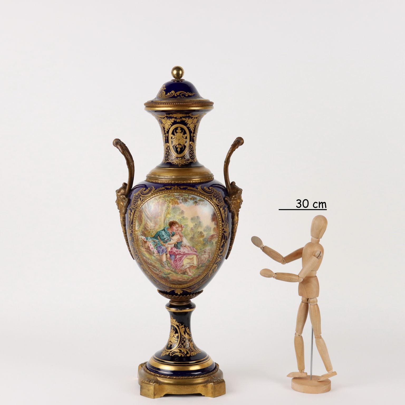 Cobalt blue ceramic vase mounted on gilt bronze with female-headed handles. Rich gold decorations with leafy scrolls and plant motifs. In the reserves there are paintings with an amorous scene and a lake landscape.