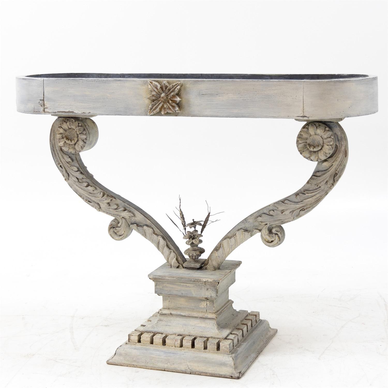 Jardinière set in a light grey color with an oval-shaped planter on carved rocaille supports above a square, multi-stepped pedestal with dentils. In the centre a small flower bouquet of tin and wire. With a tin basin.