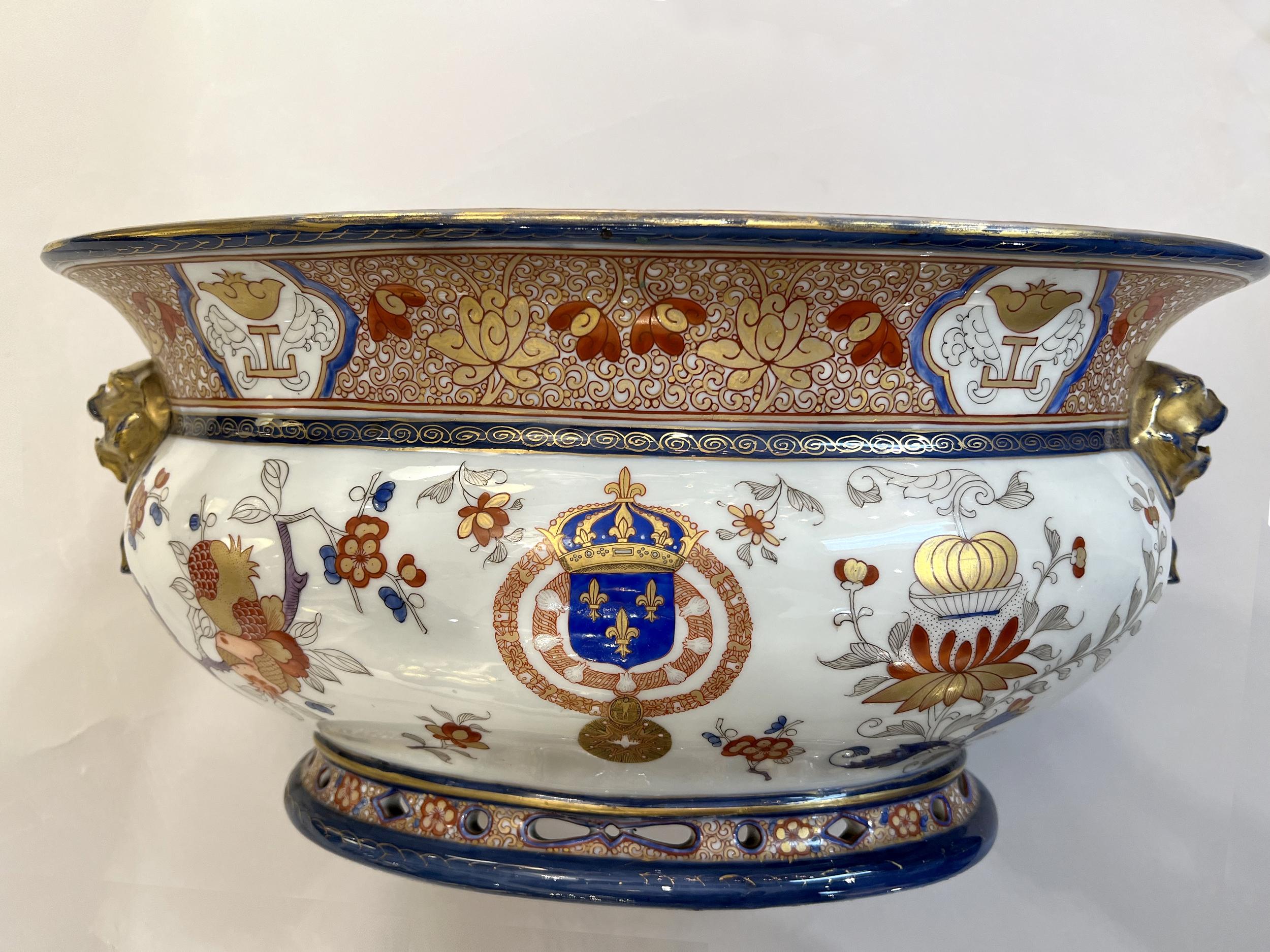 Refresher stand or jardinière with the royal coat of arms of France.
In porcelain in the spirit of the Compagnie des Indes, oval with two chimera-shaped handles, with polychrome and gold decoration of pomegranate branches, chrysanthemums and fruit,