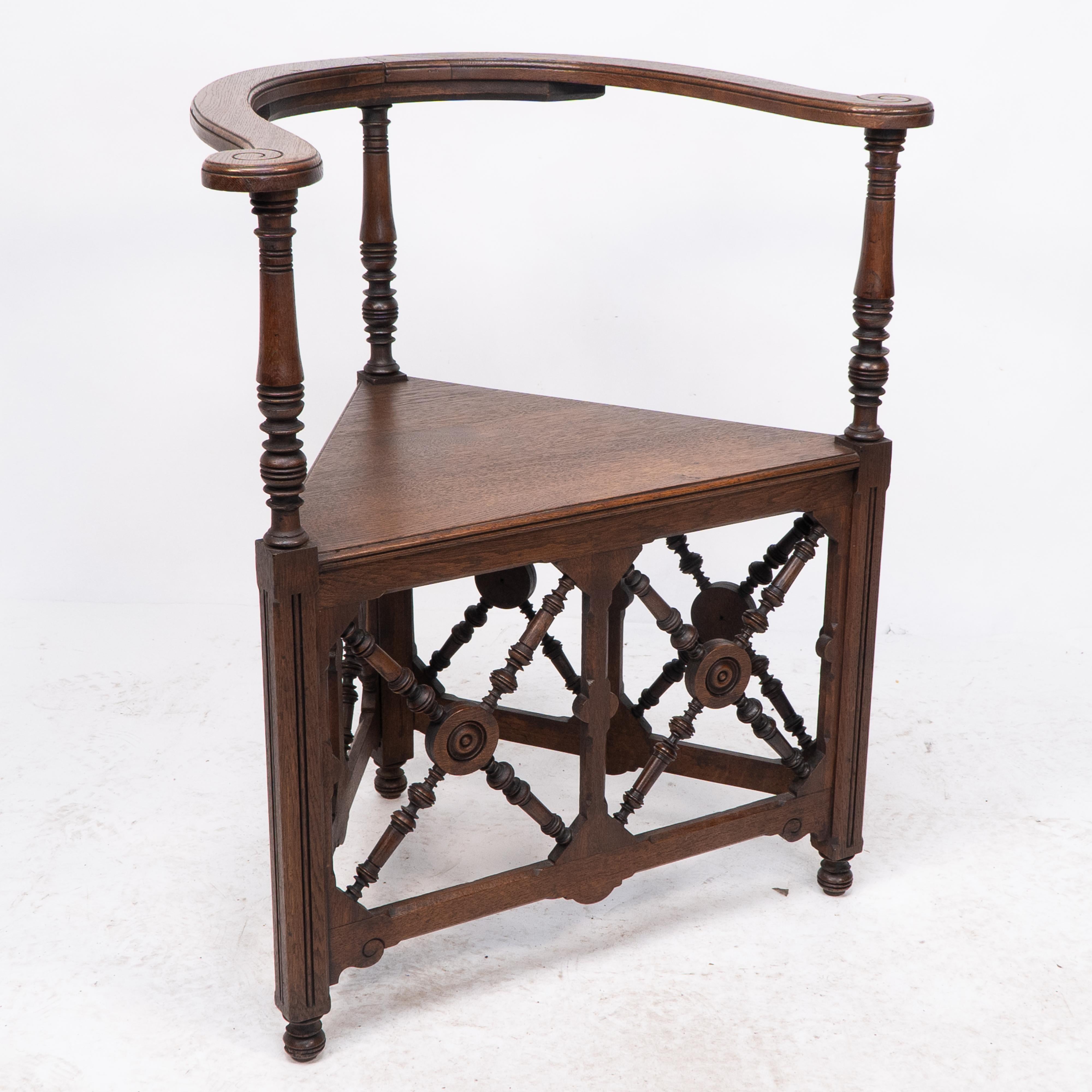 Jas Shoolbred. 
An exceptional English Aesthetic Movement oak corner armchair with wrap-around arms with incised scrollwork decoration to the top of the arm ends with turned supports below and tramline details to the legs, a triangular seat with