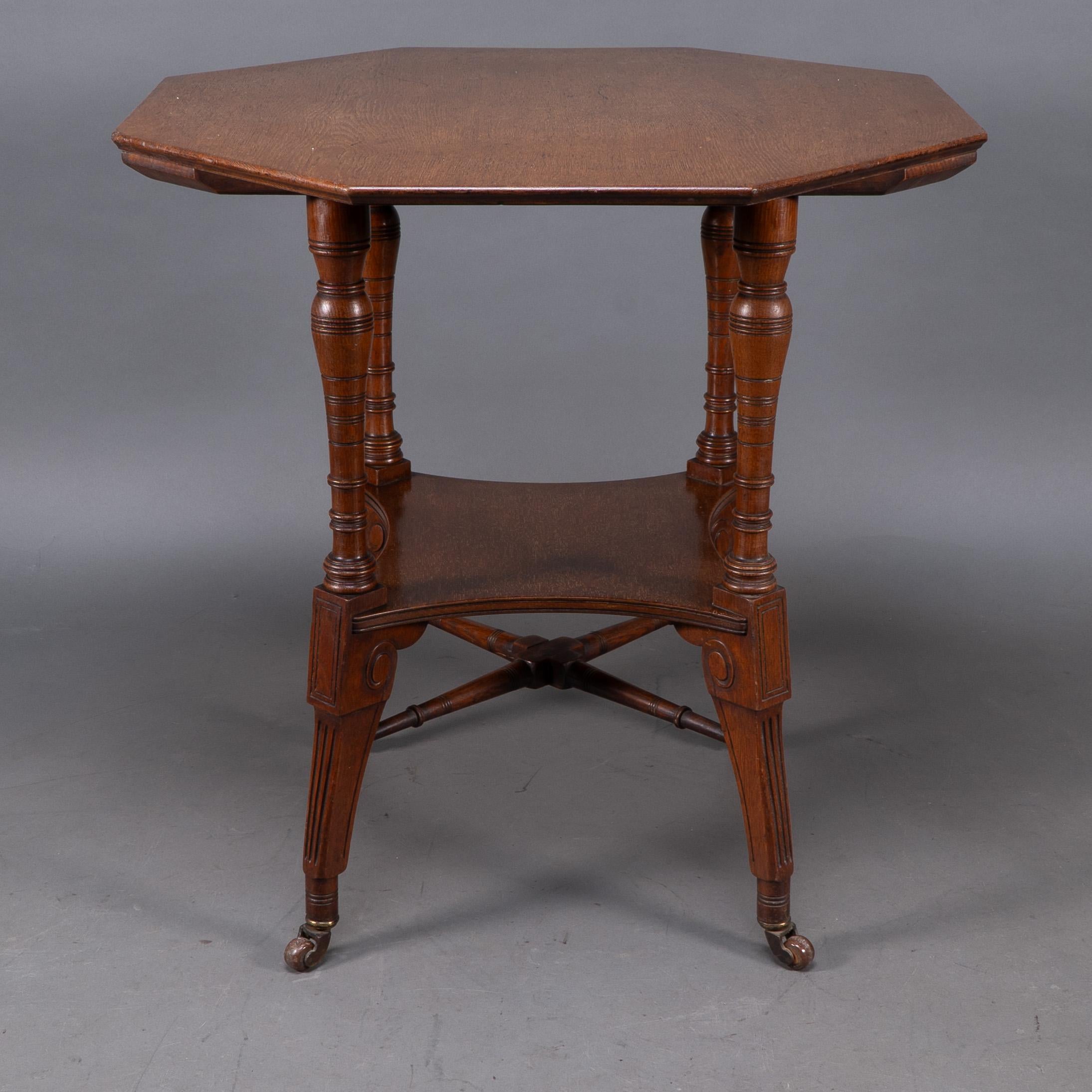 Jas Shoolbred. An octagonal walnut center table with central shelf, carved circular scroll details to the legs on castors, united by lower cross stretchers.