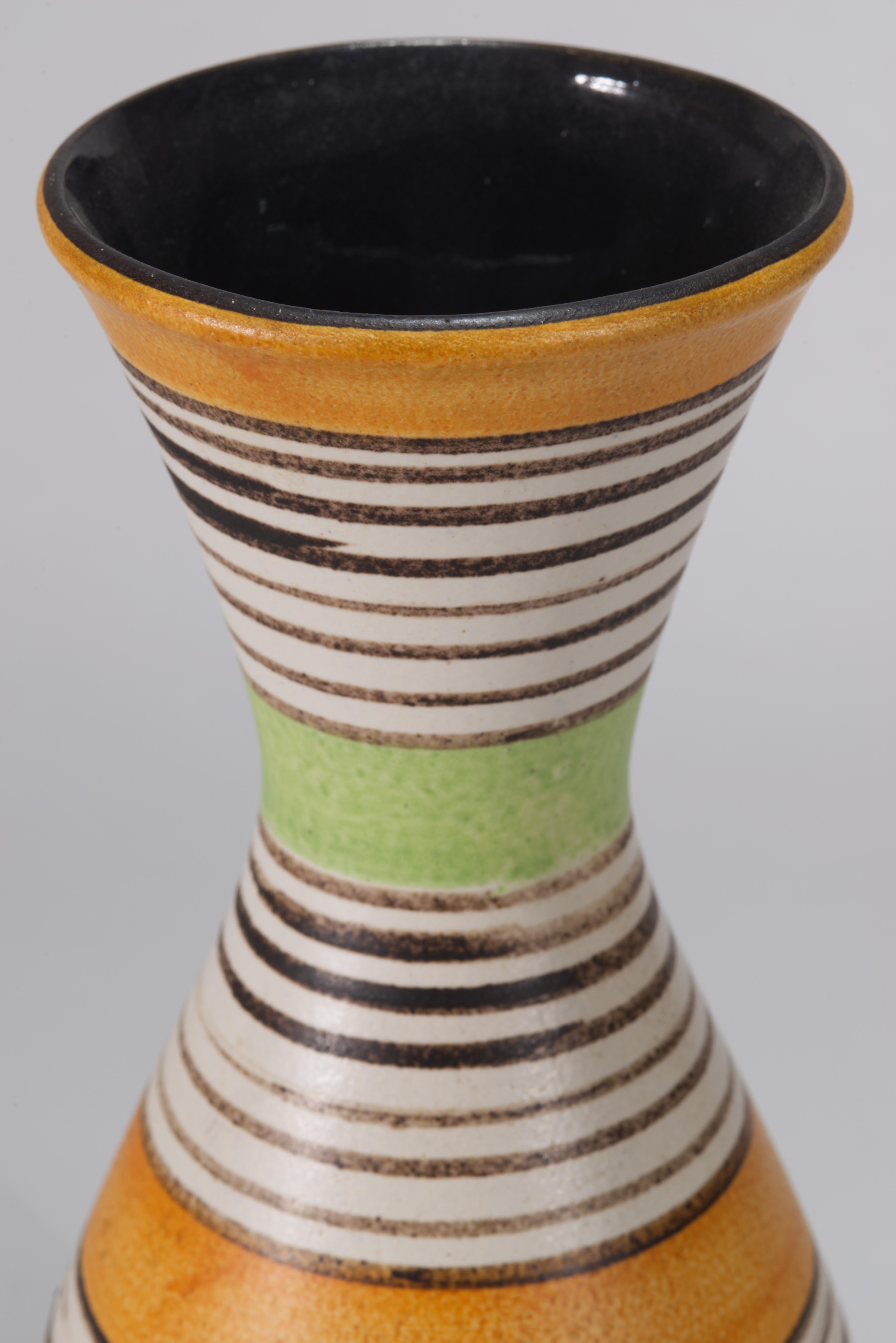 Il vaso in ceramica Mid Century Modern presenta un decoro grafico astratto che avvolge l'intero corpo del vaso con bande colorate di verde e arancione divise da strisce bianche e grigio scuro. La direzione e il posizionamento del decoro accentuano