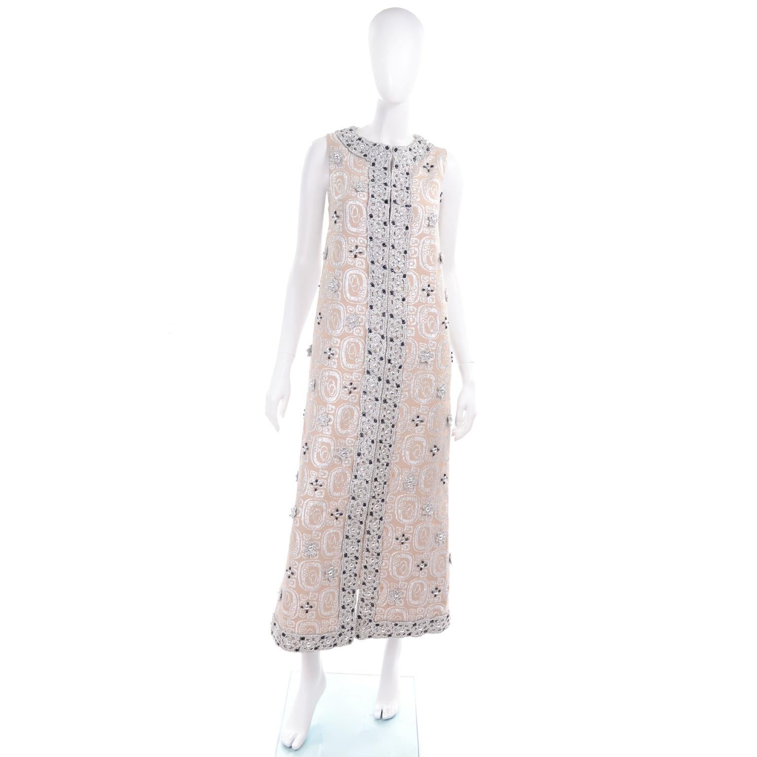 This beautiful 1960's evening gown is sleeveless and the cream silk and silver lurex fabric is covered with gorgeous beaded and braided metallic flowers and rhinestones. The dress is lined in pure silk and has hidden hooks and eyes up the front for