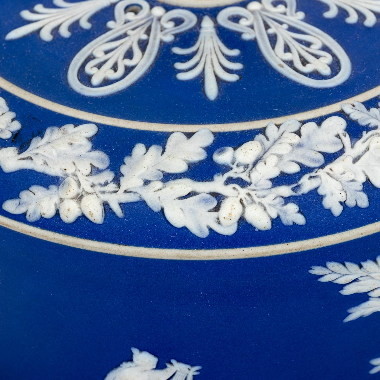 Dark blue jasperware cheese dome with classical figures all around, circa 1900. Raised florals and acorns. Not signed. Heavy. Made in England possibly Wedgwood. Please note of wear consistent with age including paint loss and finish loss. 10 LBS.