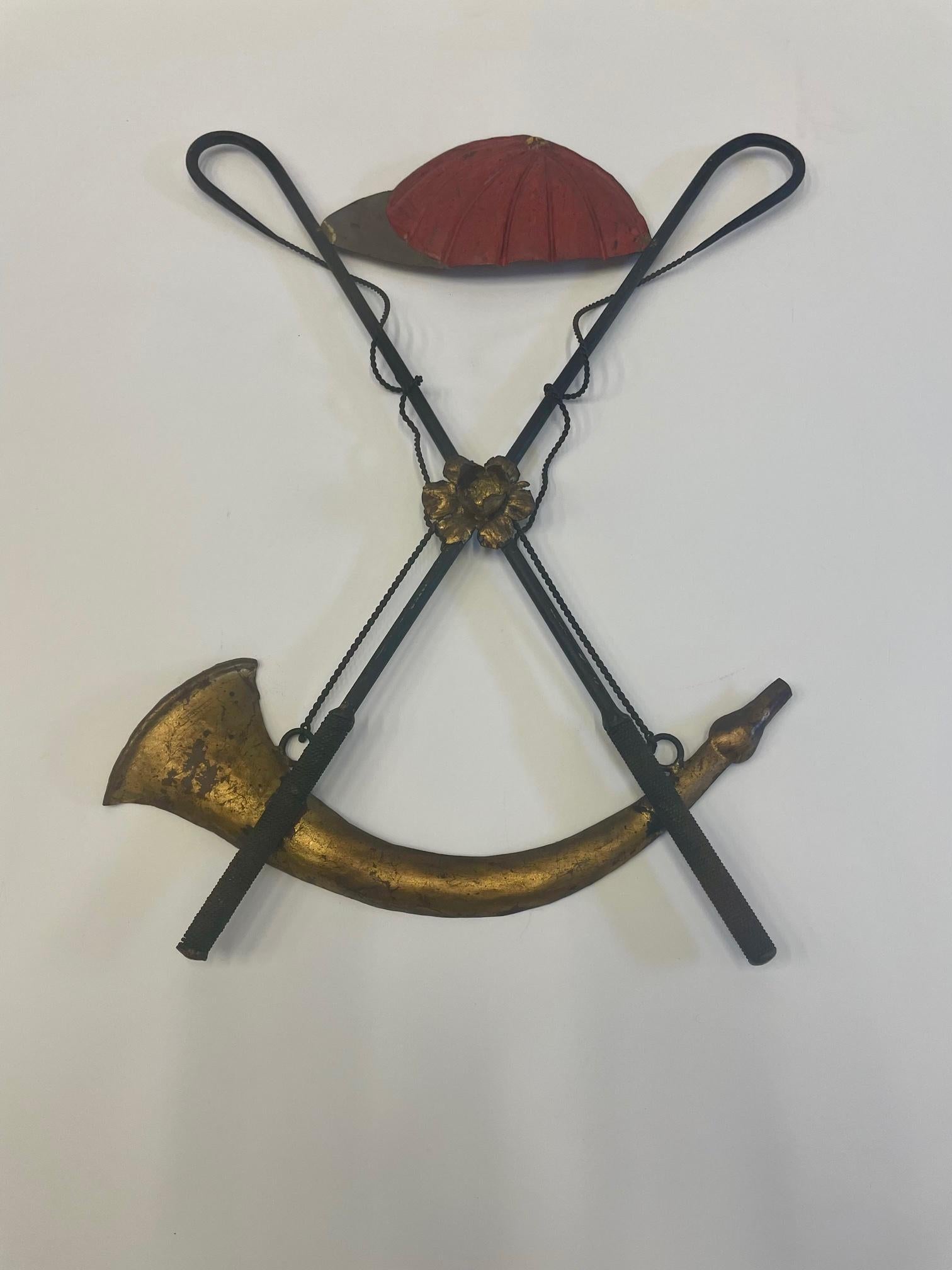 A rare and special iron wall sculpture with equestrian motif having red painted jockey hat, criss crossed rider's crops and a perfectly situated gilded crescent shaped horn adorning the bottom.
