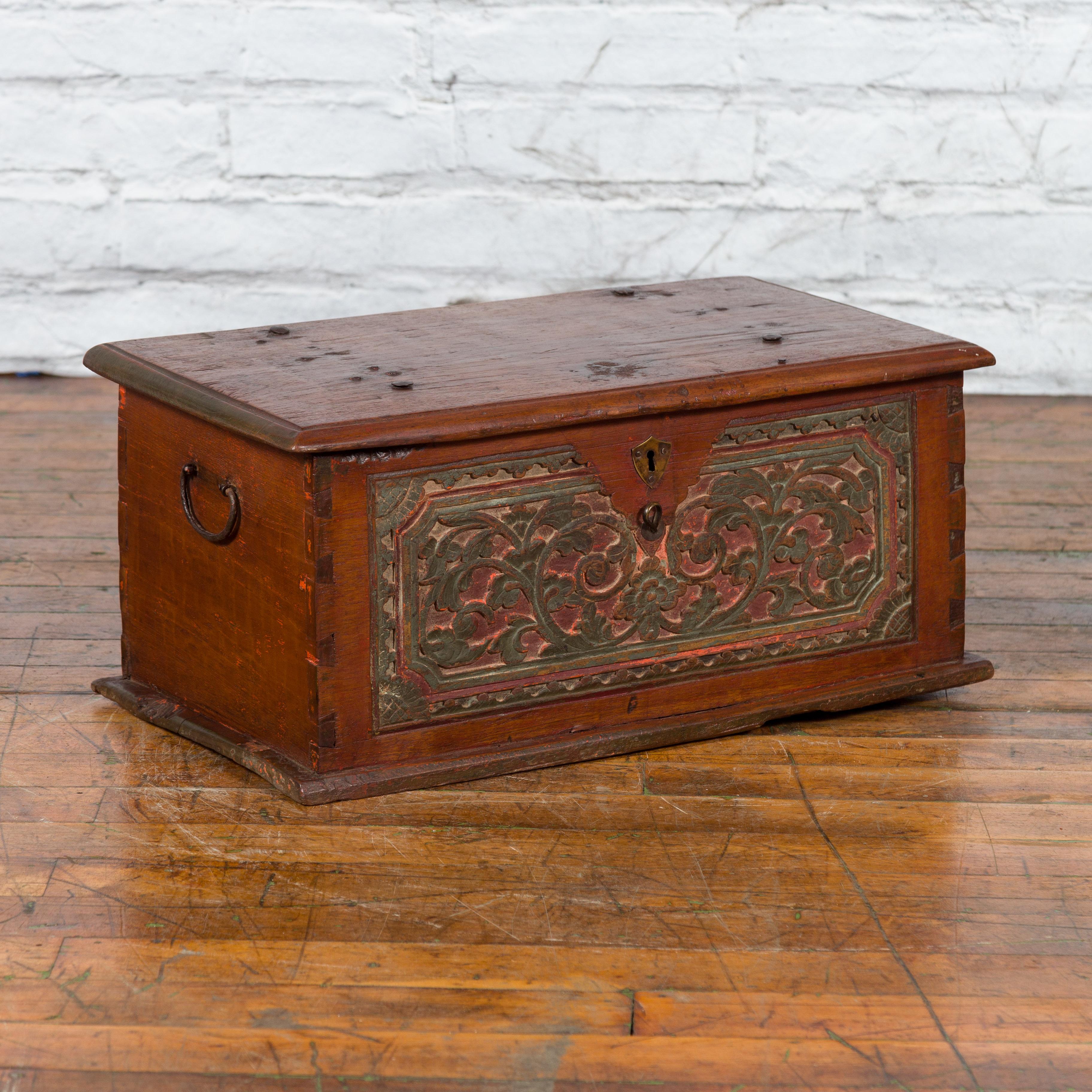 A Javanese teak wood trunk from the 19th century with carved scrolling foliage, green and red painted accents, shield-shaped escutcheon and dovetail construction. Created on the island of Java in the 19th century, this teak (a very sturdy wood)