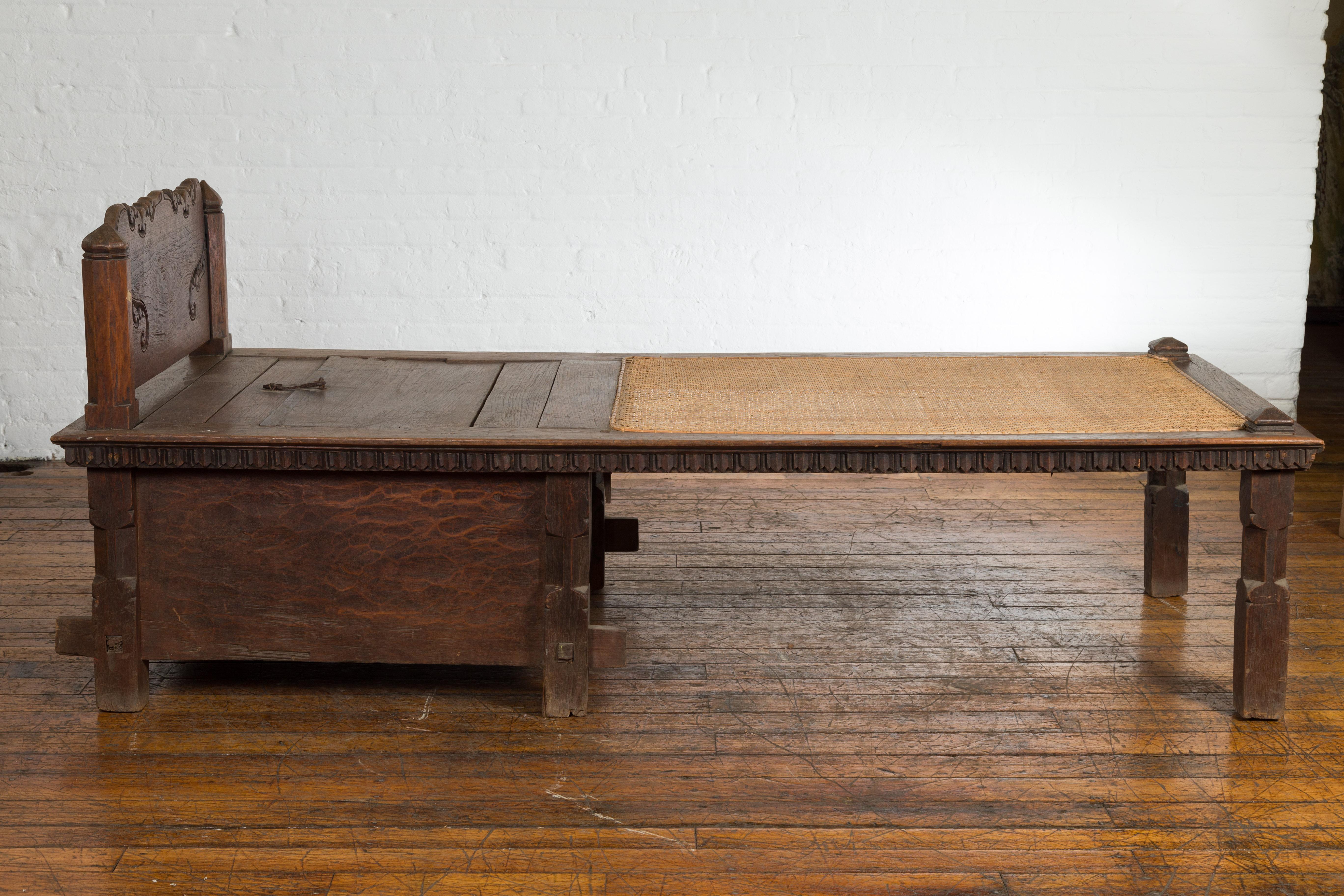 An antique Javanese teak wood daybed from the 19th century, with rattan seat, storage and hand carved scrolling motifs. Handcrafted on the island of Java during the 19th century, this teak (a very sturdy wood) daybed charmed us right away with its