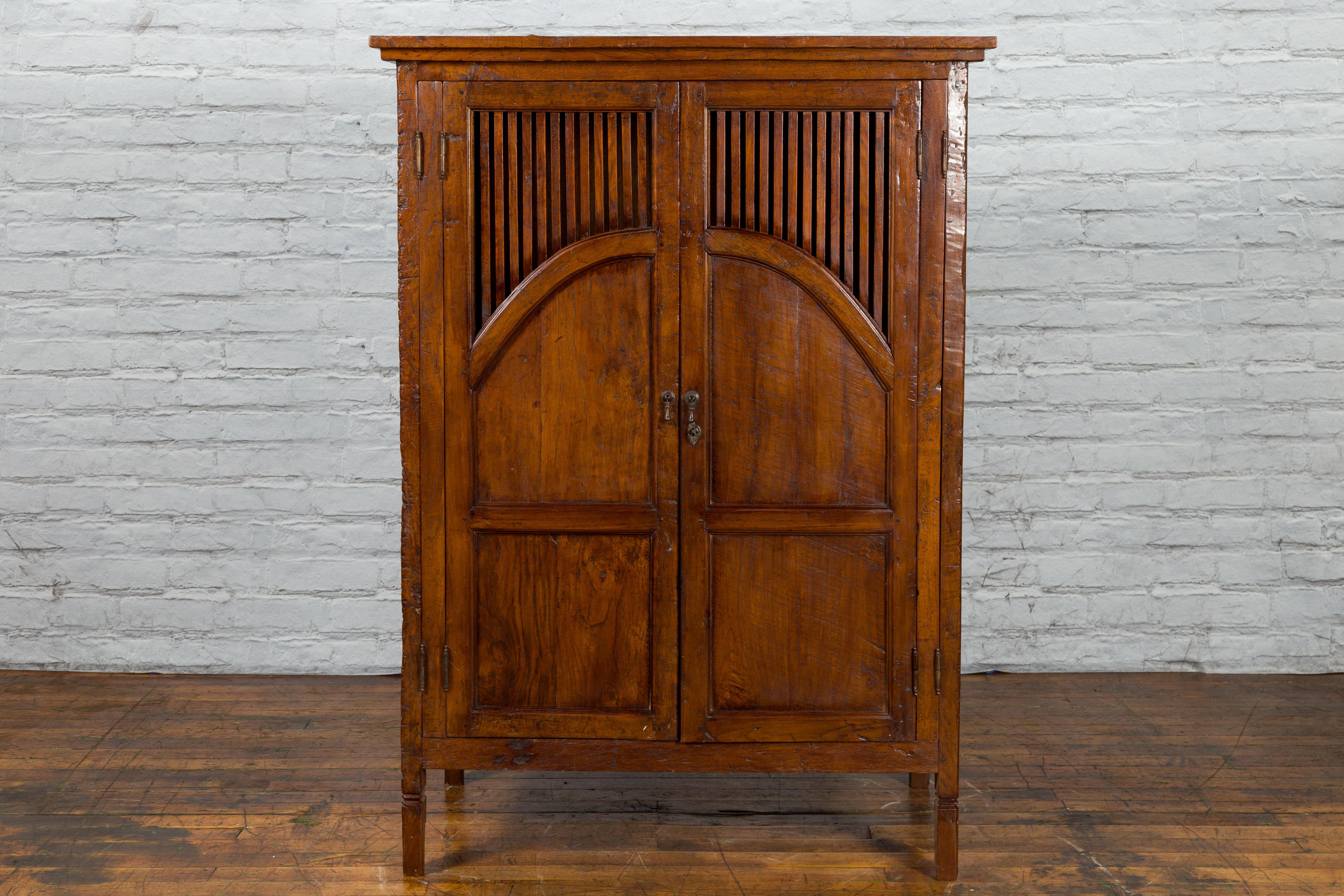 An antique Javanese hand-carved teak armoire from the early 20th century, with slatted motifs, slightly carved legs and nice patina. Created on the island of Java during the early years of the 20th century, this teak wood armoire features a linear,