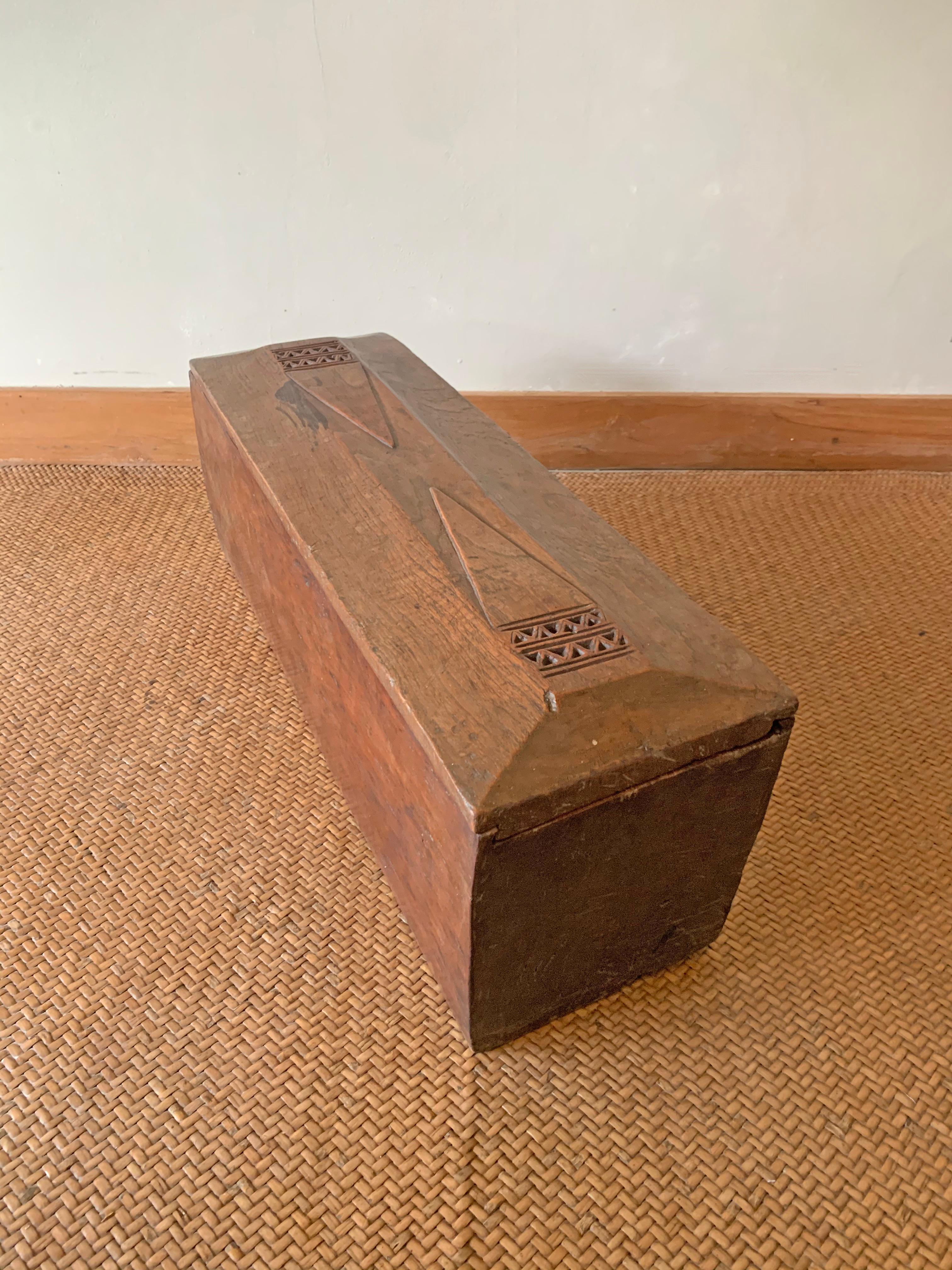 This teak storage box comes for the Island of Java, Indonesia. Dating to the Mid-20th Century it was crafted from a single block of teak. It features a sliding lid and has an elegant wood texture as well as wood engravings. There are some chips and