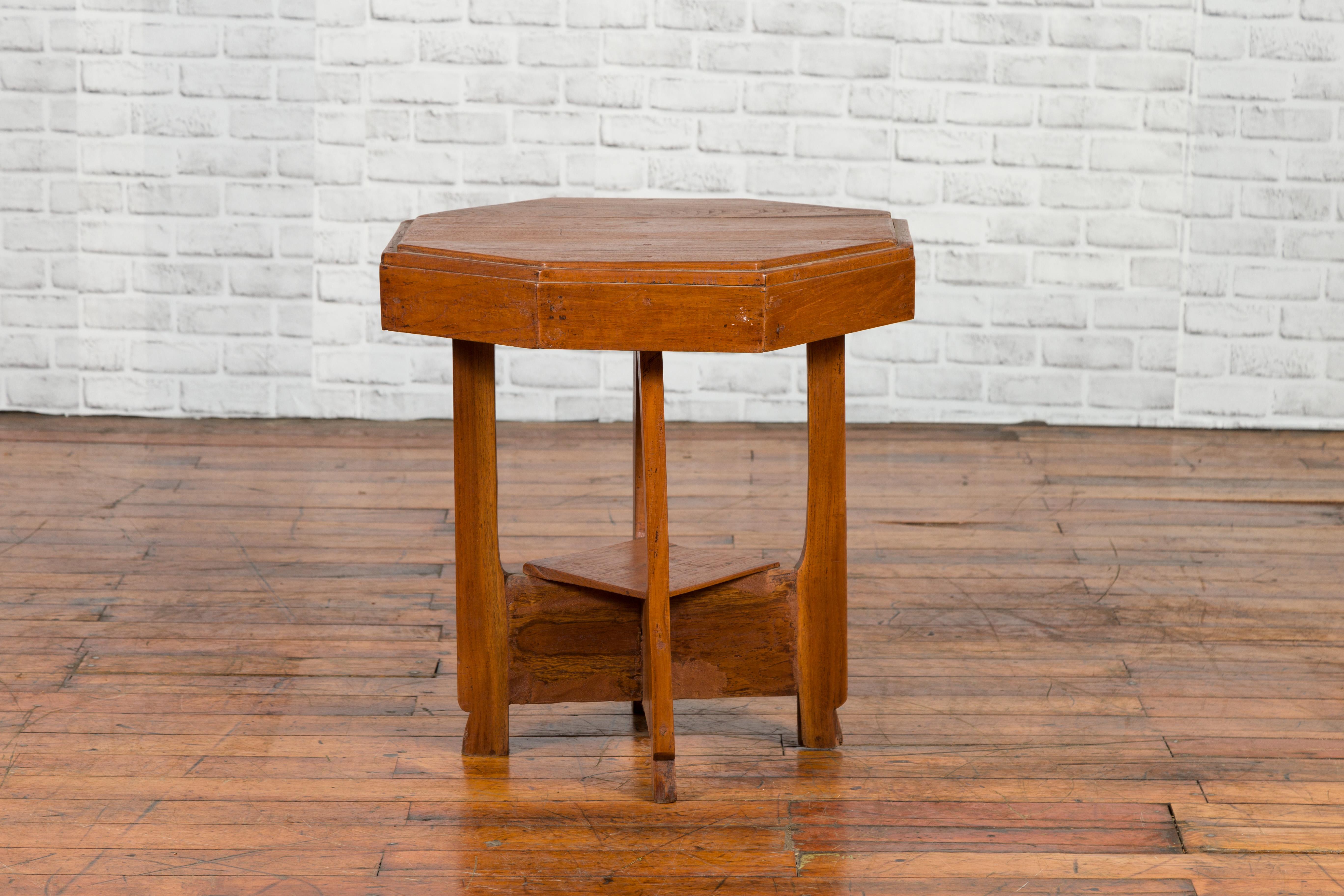 A Javanese teak Art Deco style table from the mid 20th century with octagonal top, beveled accents and lower shelf. Created in Java during the midcentury period, this vintage teak Art Deco table features an octagonal, slightly raised top, sitting