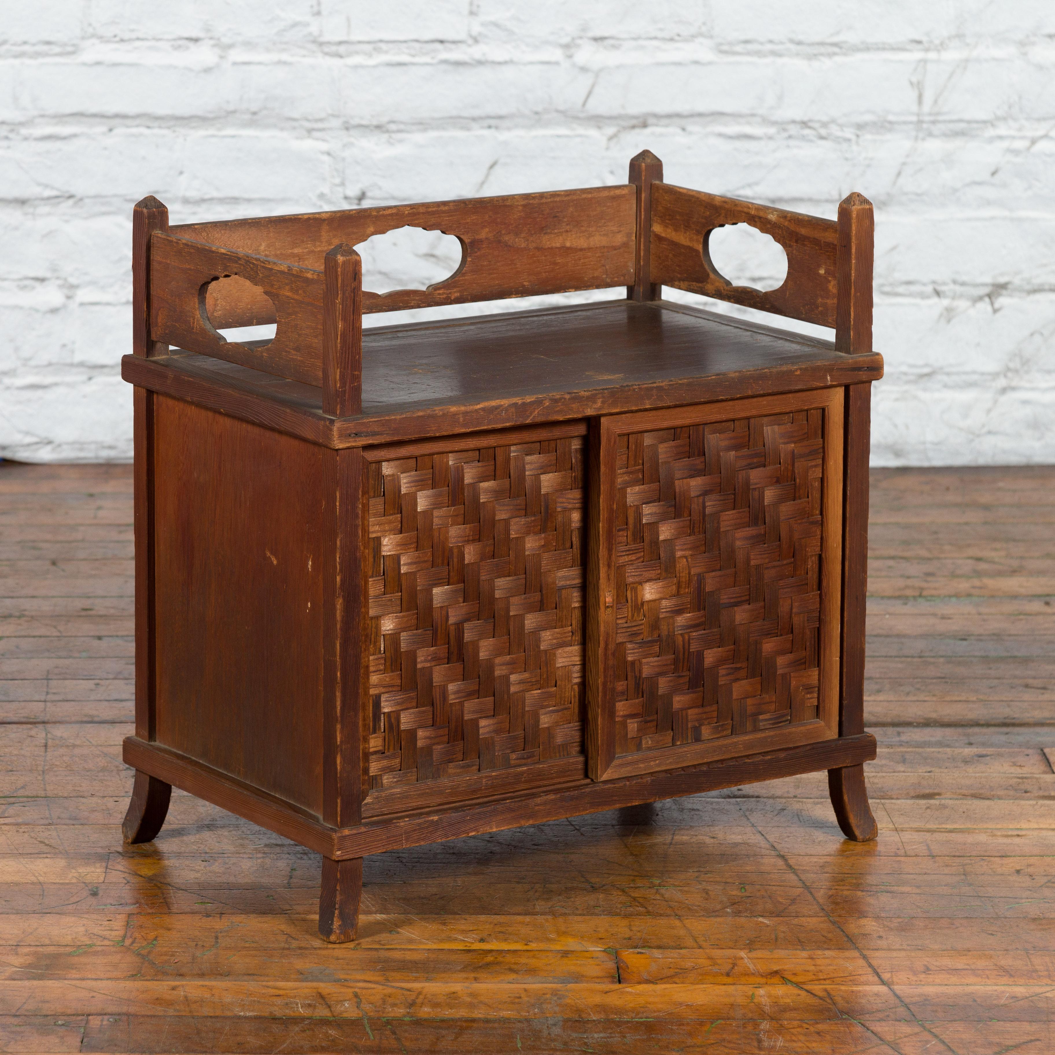 A vintage Javanese wooden side cabinet from the mid 20th century with latticed bamboo sliding doors, three-quarter gallery, pierced motifs and slightly curving feet. Created on the island of Java during the Midcentury period, this side cabinet