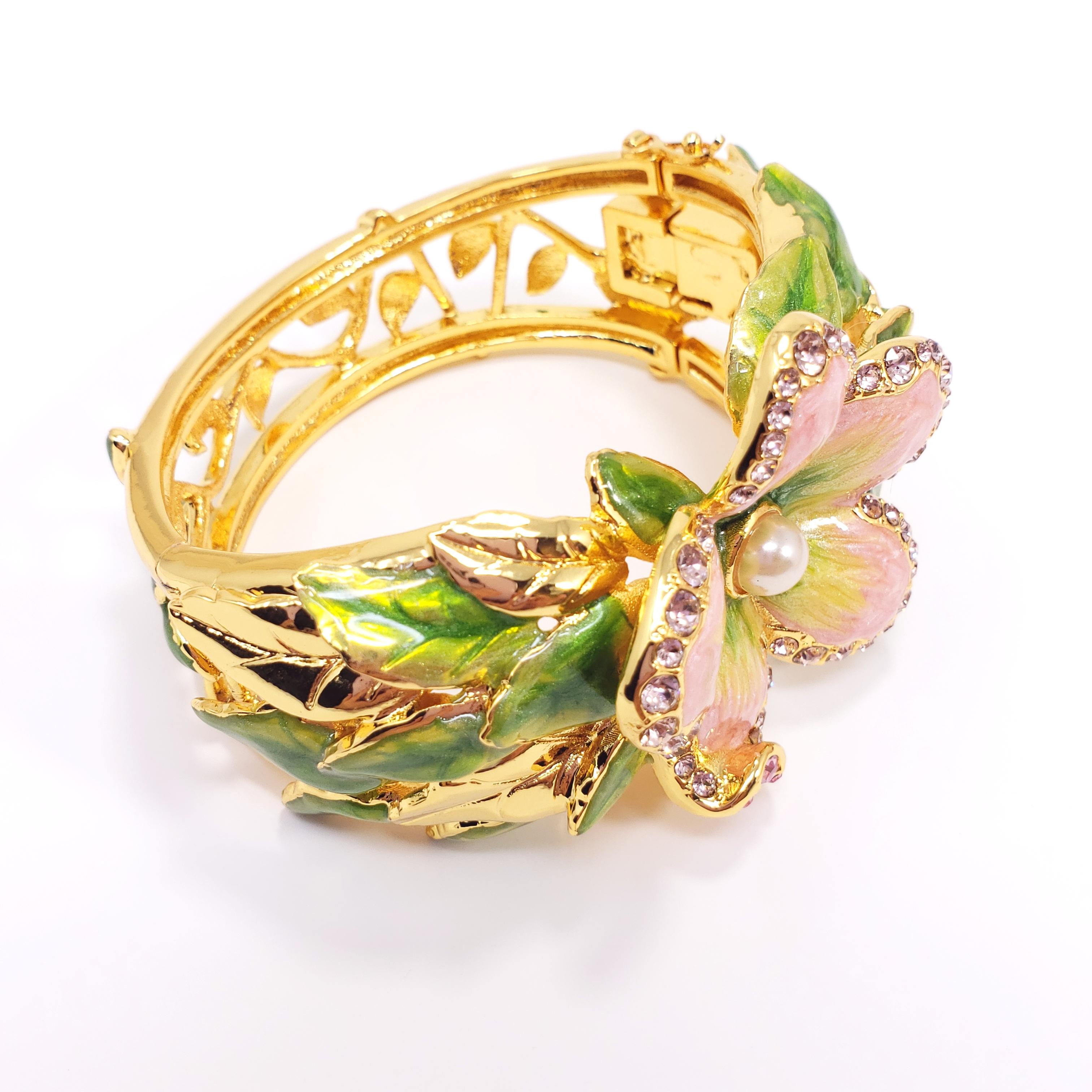 Flower power! An ornate floral bracelet pink crystals, green and violet enamel, and a single faux pearl. The central flower sits upon layers of leaves on each side.

Dimensions: Height 4 cm / 1.6 in, inner diameter at widest part 6 cm / 2.36 in,