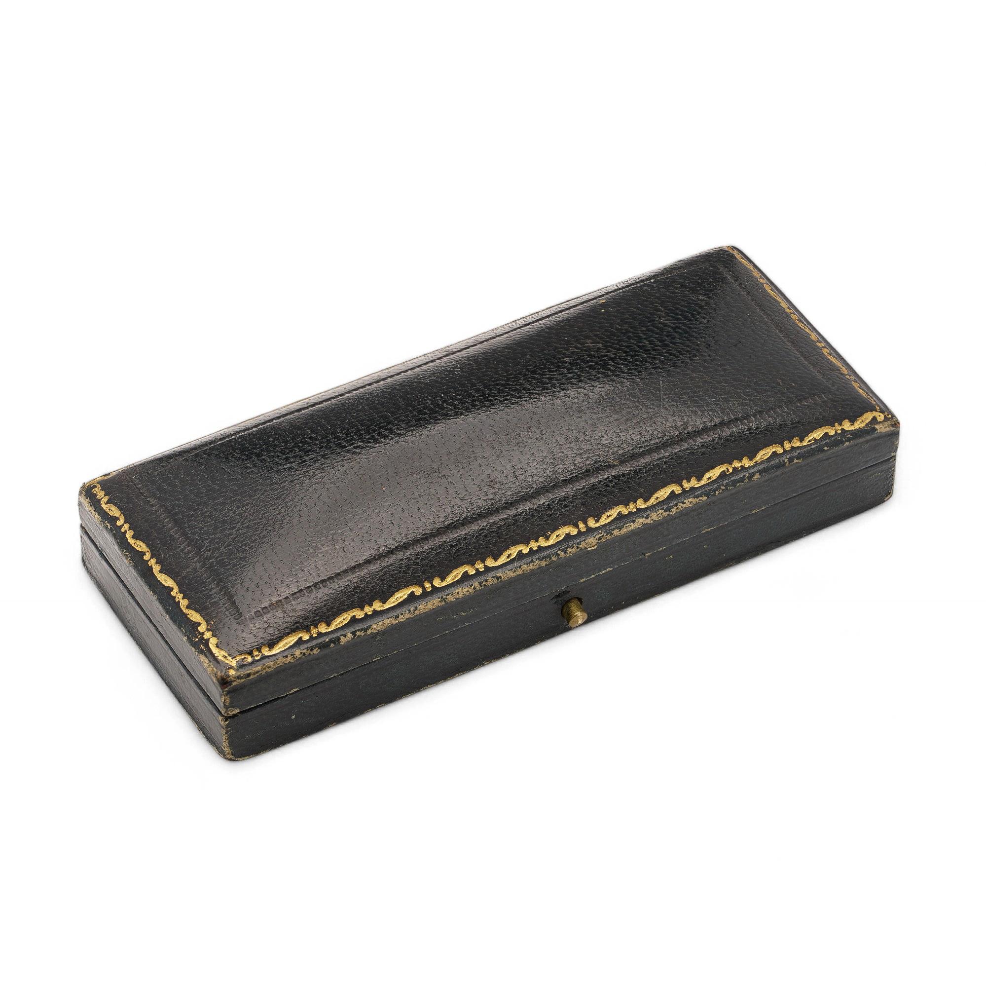 A slim rectangular brooch box with a textured exterior and a velvet-lined interior. The lid features the retailer’s name and location, adding historical charm.

A textured vintage brooch box by J.B.G. Peters with a velvet-lined interior. Its