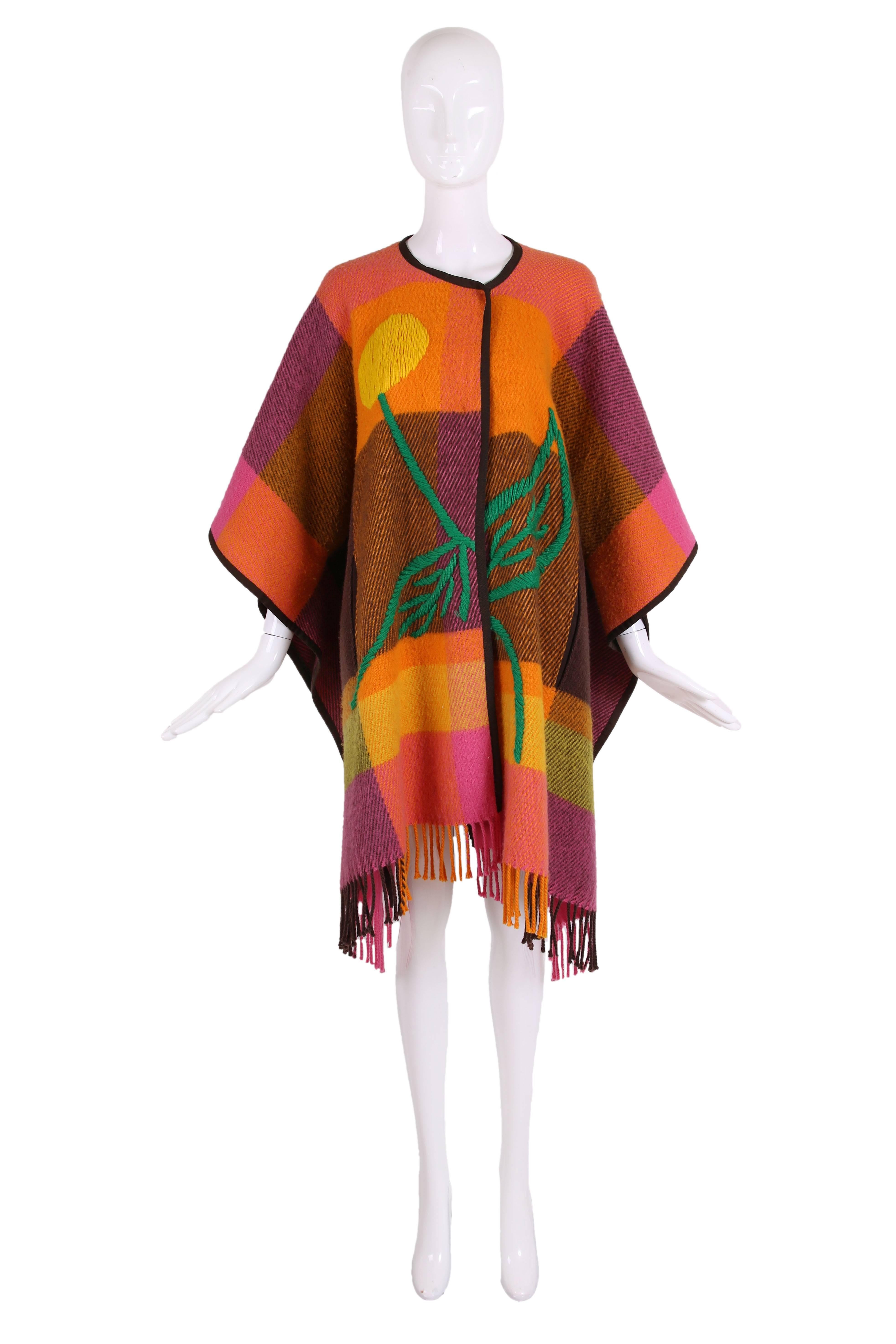 JC de Castlbajac pink, yellow, orange, green and brown plaid melton wool poncho w/embroidered flower across center front and brown grosgrain trim. Poncho has interior snap closure and button closure, hidden pockets and fringe trim at hem. In