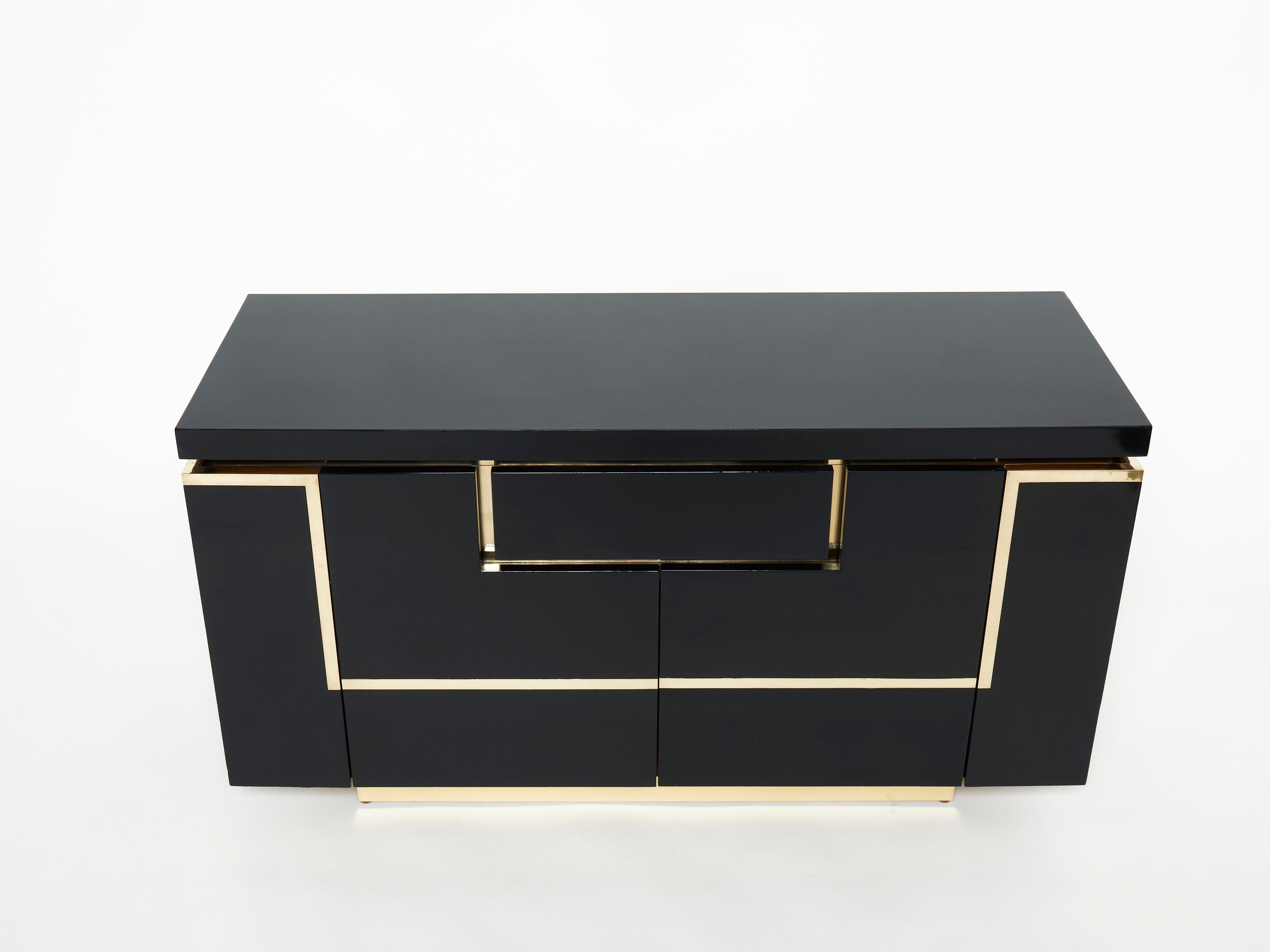 A timeless vintage piece, this mid-century cabinet bar sideboard feels imposing and glamourous, with thick, straight lines of brass adorning its exterior of reflective black lacquer. Glossy black lacquer, paired with bright brass accents, feels