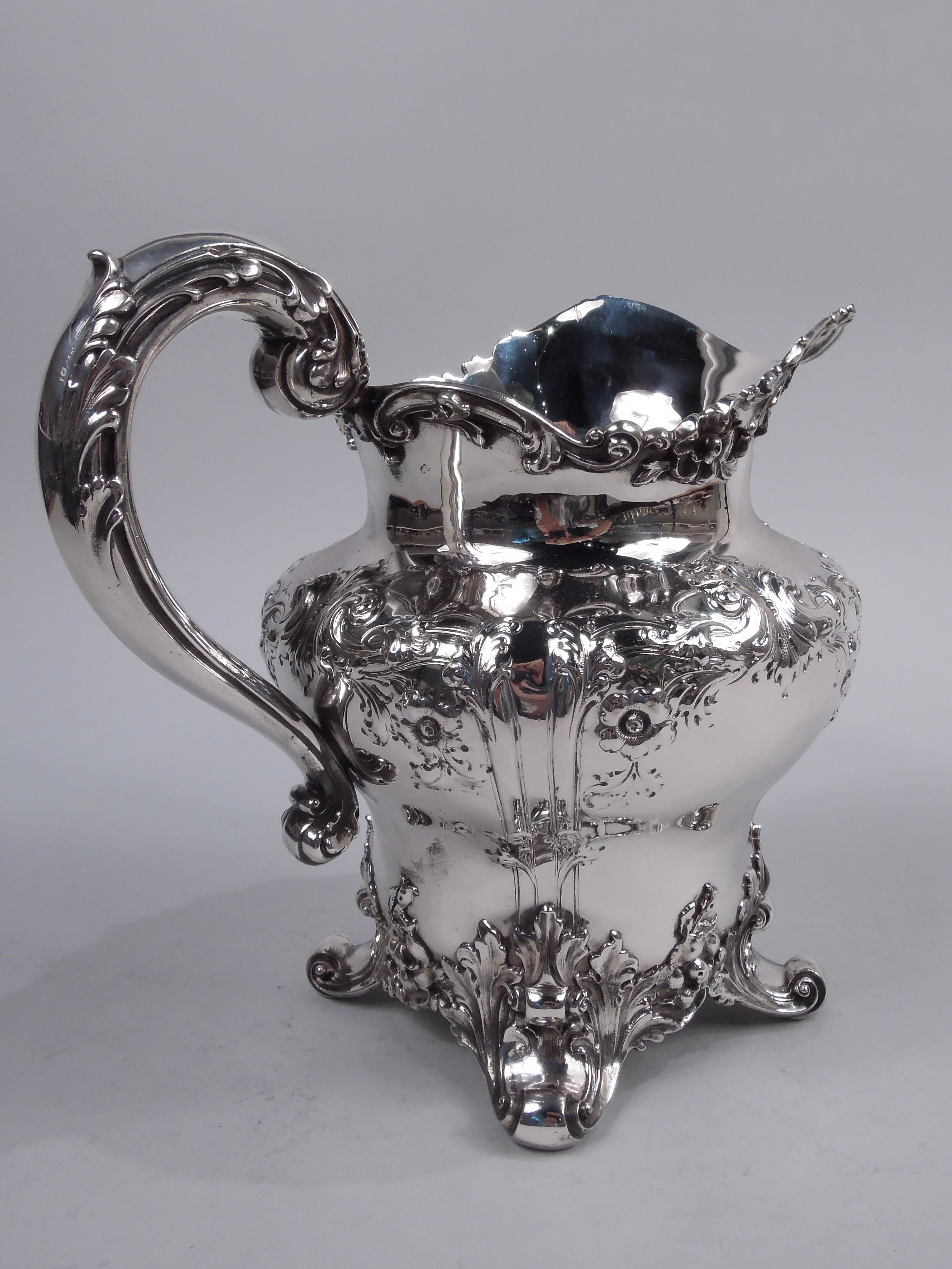 Pretty Edwardian Classical sterling silver water pitcher. Made by Graff, Washbourne & Dunn in New York, ca 1910. Wide-bodied baluster with helmet mouth, leaf-capped high-looping handle, and 4 leaf-mounted volute scroll supports. Chased frames