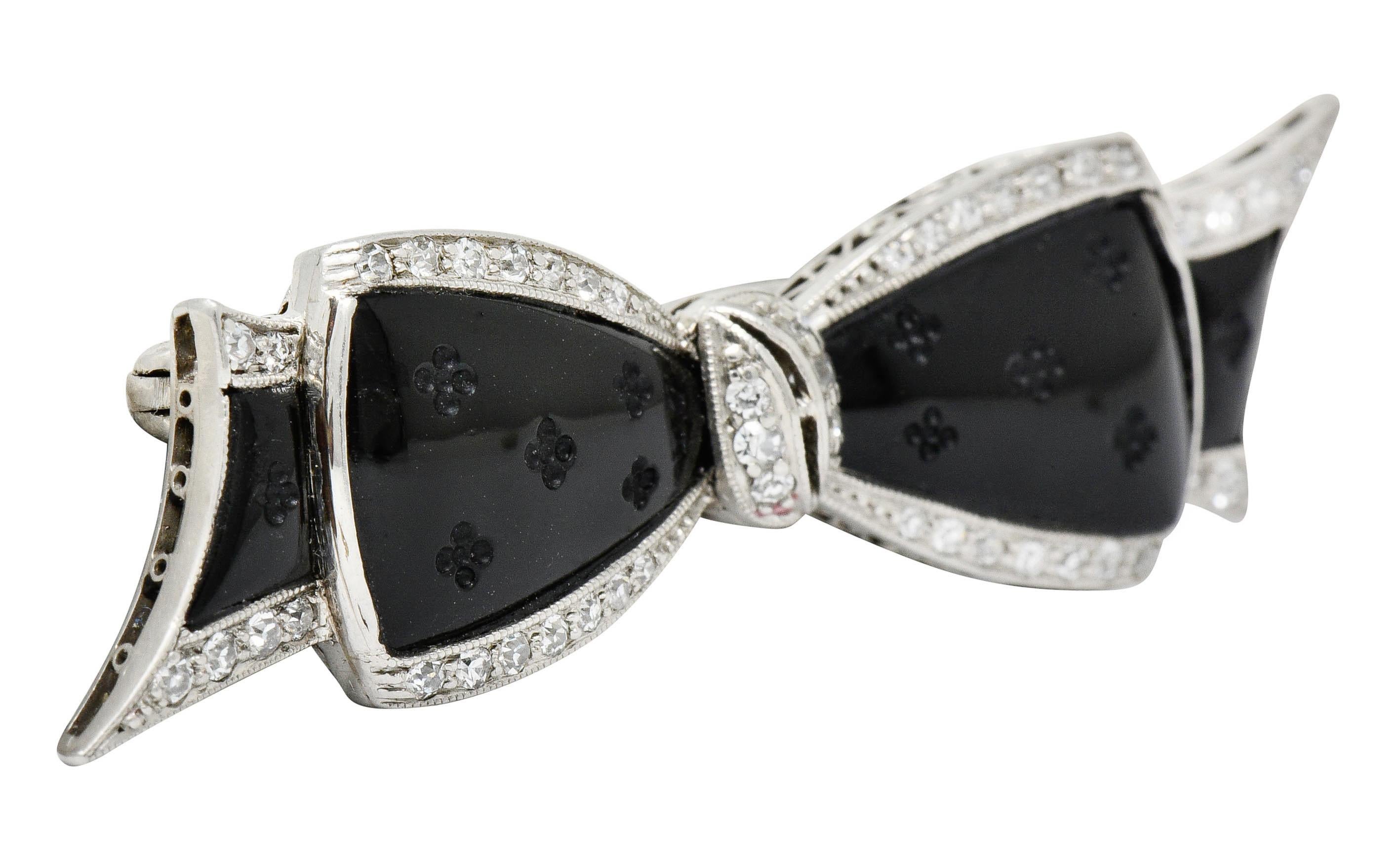 Brooch is designed as a stylized bow with a milgrain platinum frame decorated with a pierced and ornately scrolled gallery

Centering calibré cut onyx, as a bow motif, deeply engraved with a floral pattern

Accented throughout by single cut diamonds