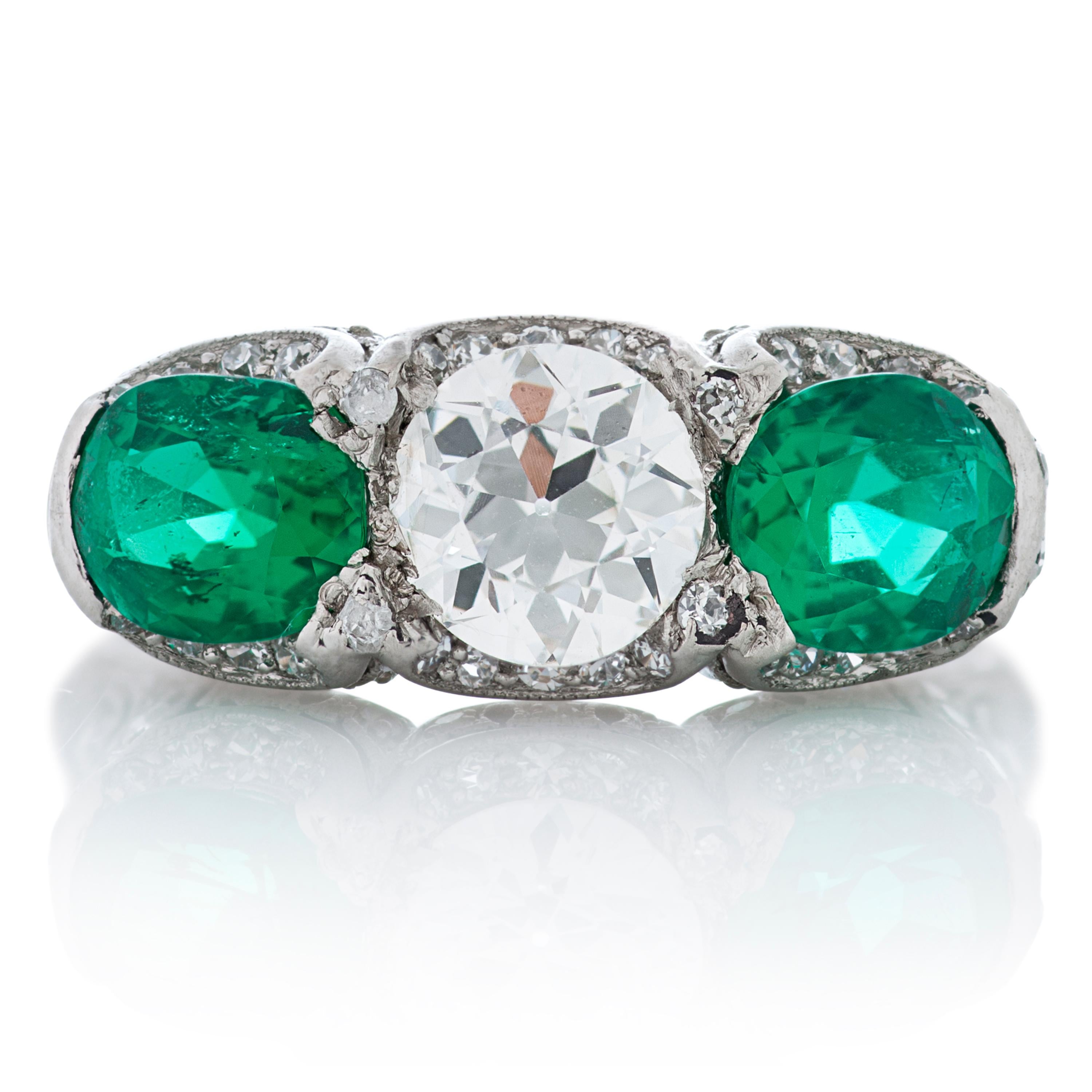 J. E. Caldwell & Co. Art Deco platinum emerald and diamond ring.  Two cushion cut emeralds weighing a total of 1.37 carats are set on either side of one Old European Cut diamond weighing 0.84 carat with estimated G color and VS clarity.  The ring is
