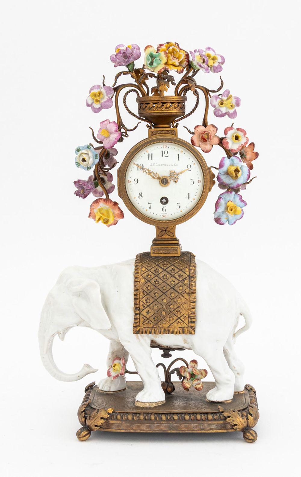J. E. Caldwell and Company Bronze and Porcelain Clock and Garniture Three-Piece Set, 19th century, comprising: circular vase form clock with painted porcelain flowers atop a white porcelain elephant mounted on bronze rectangular base on four acorn