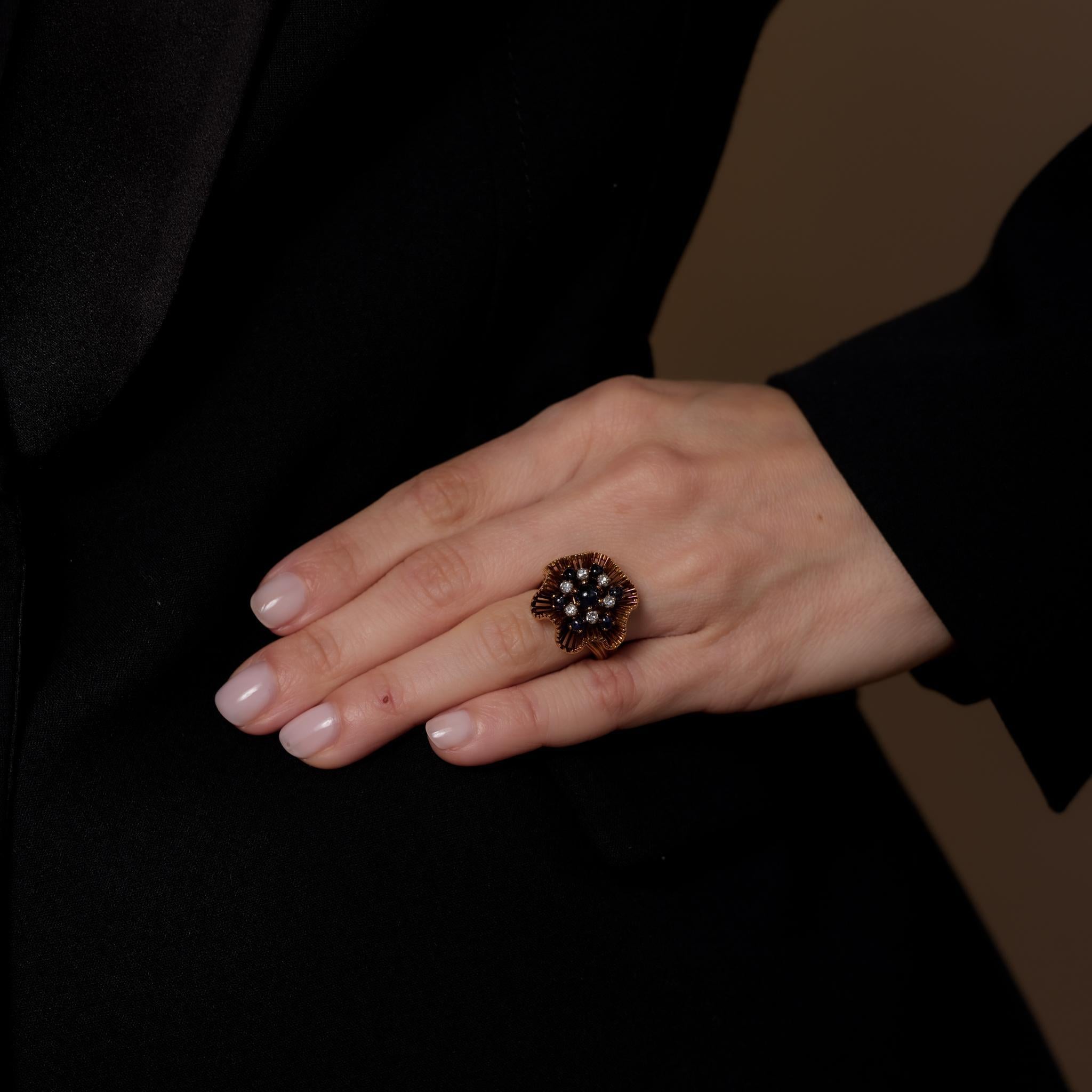 This Retro JE Caldwell 18k yellow gold cocktail ring showcases seven cabochon cut blue sapphires totaling 1.70 carats, accented by six single cut diamonds weighing .25 carats, G-H color, and SI clarity. Signed and crafted in the 1940s, it weighs