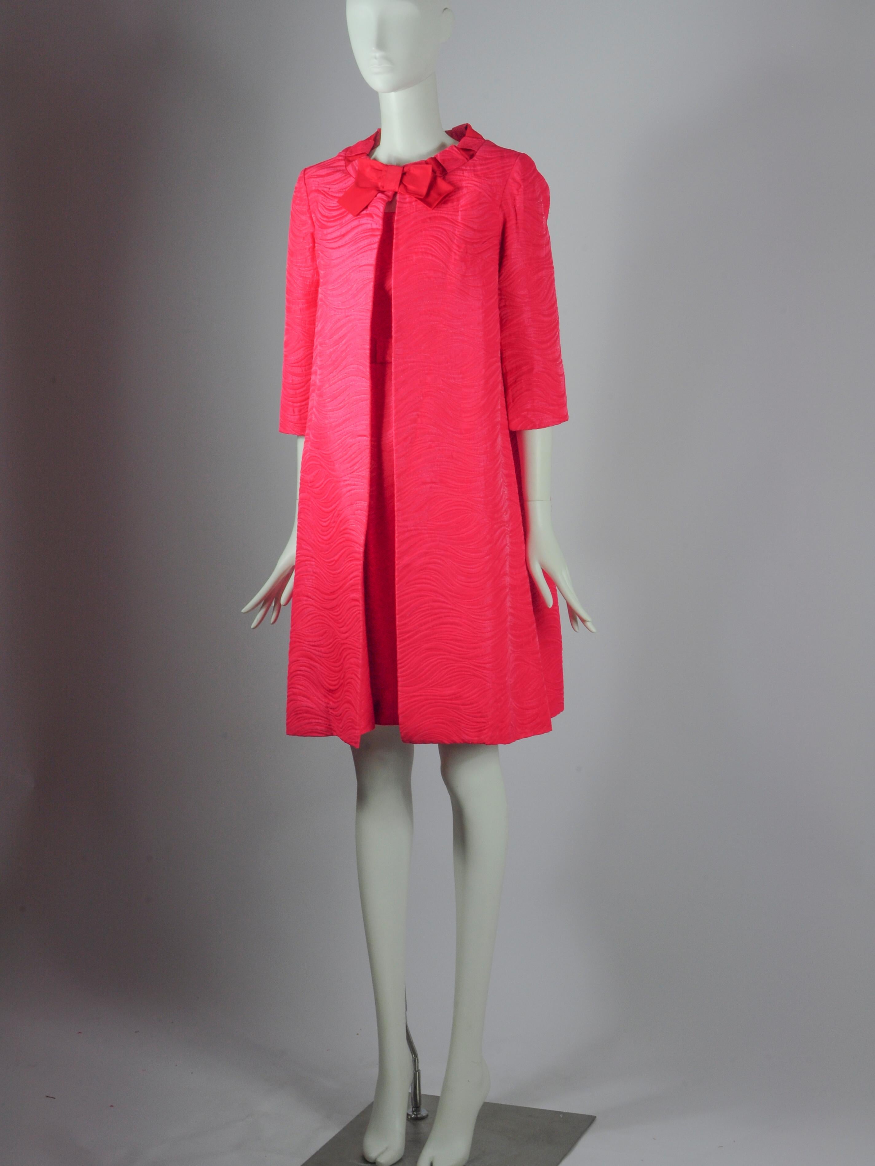 Ensemble deux pièces vintage Jean Allen London composé d'une veste et d'une robe sans manches en rose fuchsia avec détails de nœuds. Il s'agit d'un beau tissu structuré avec un motif de vagues et un léger fil métallique tissé. Elle a un air de