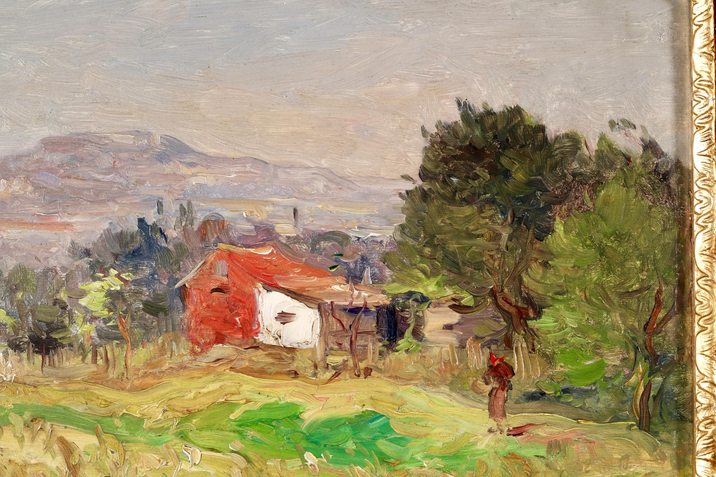 Signed figure in landscape oil on panel circa 1890 by French impressionist painter Jean Baptiste Antoine Guillemet. The piece depicts a red farm building in a rural landscape. A woman is walking across the green field beside trees and there is a