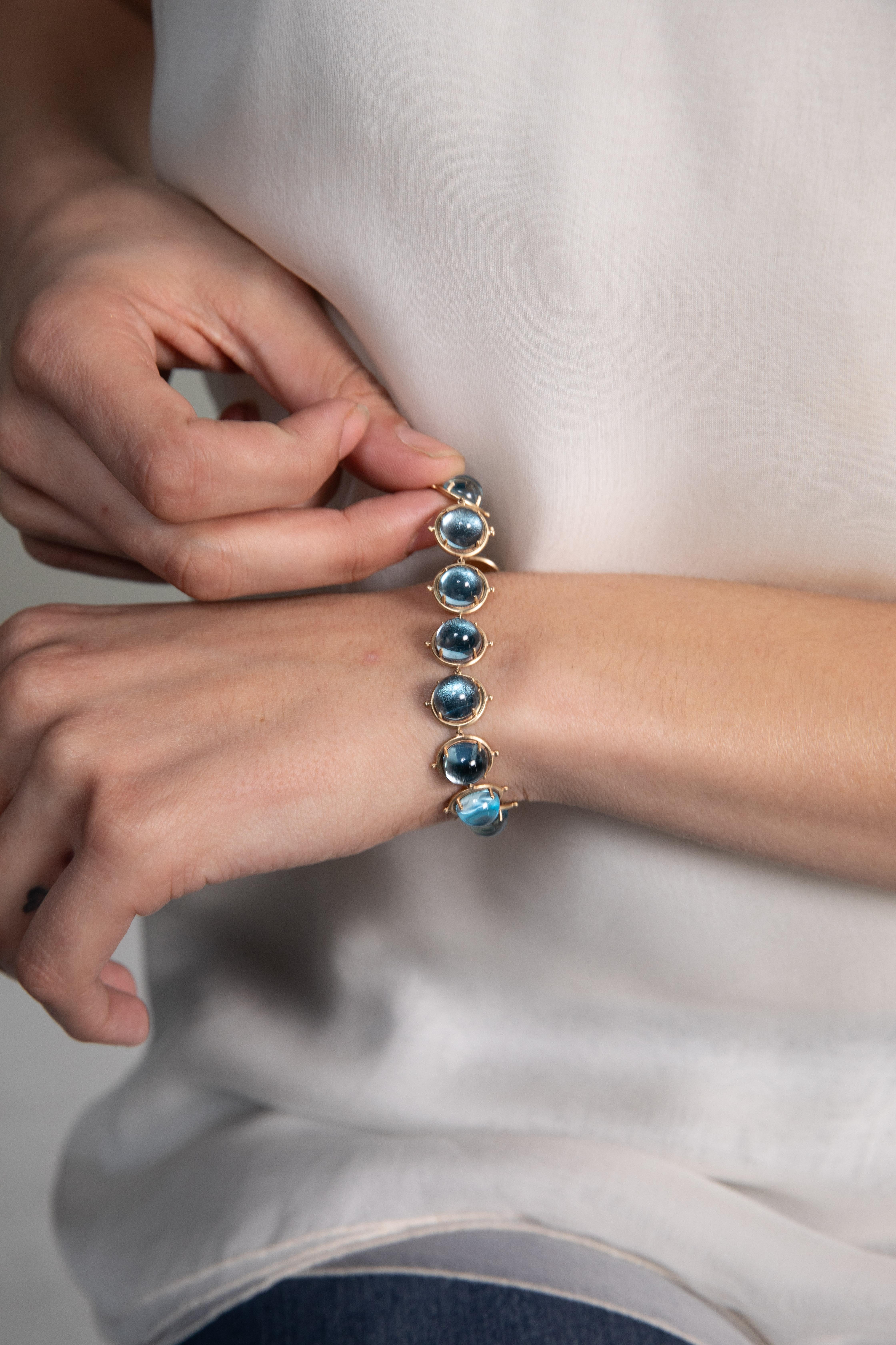 Blue Topaz round link bracelet is fashioned in 14K yellow polish gold and set with 14- 9mm topaz cabochon stones. Made in the United States in 2019.  Measures 11mm wide by 7 inches. Clasp: push clasp with a safety hook for extra protection.

