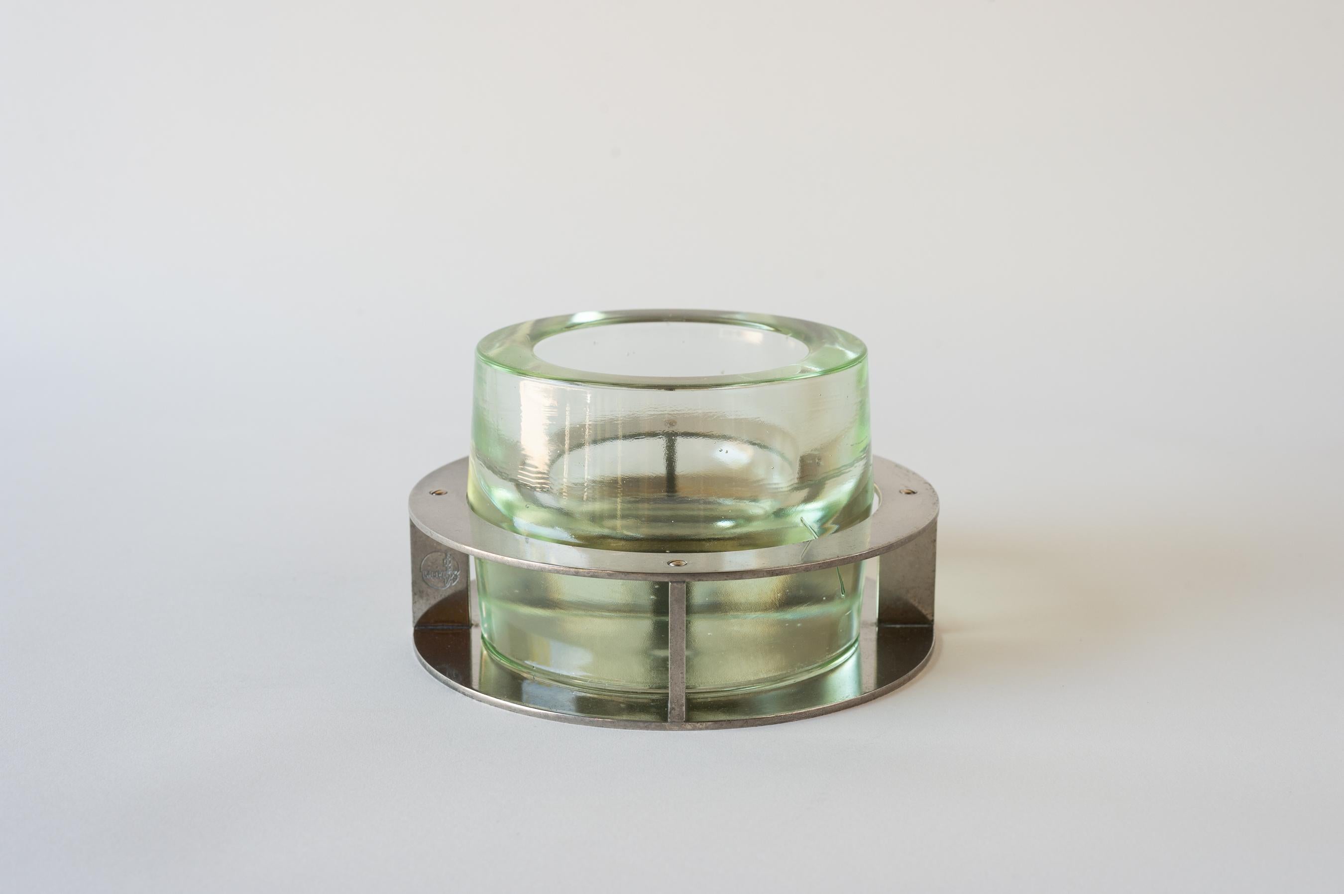 A multi-use object comprising of a thick cast glass cup and a circular metal base; to be used as a catch-all, ashtray, candy dish, candle holder or snack bowl.  During the 1930s, Jean Boris Lacroix (1902–1984) perfected the use of glass and metal,
