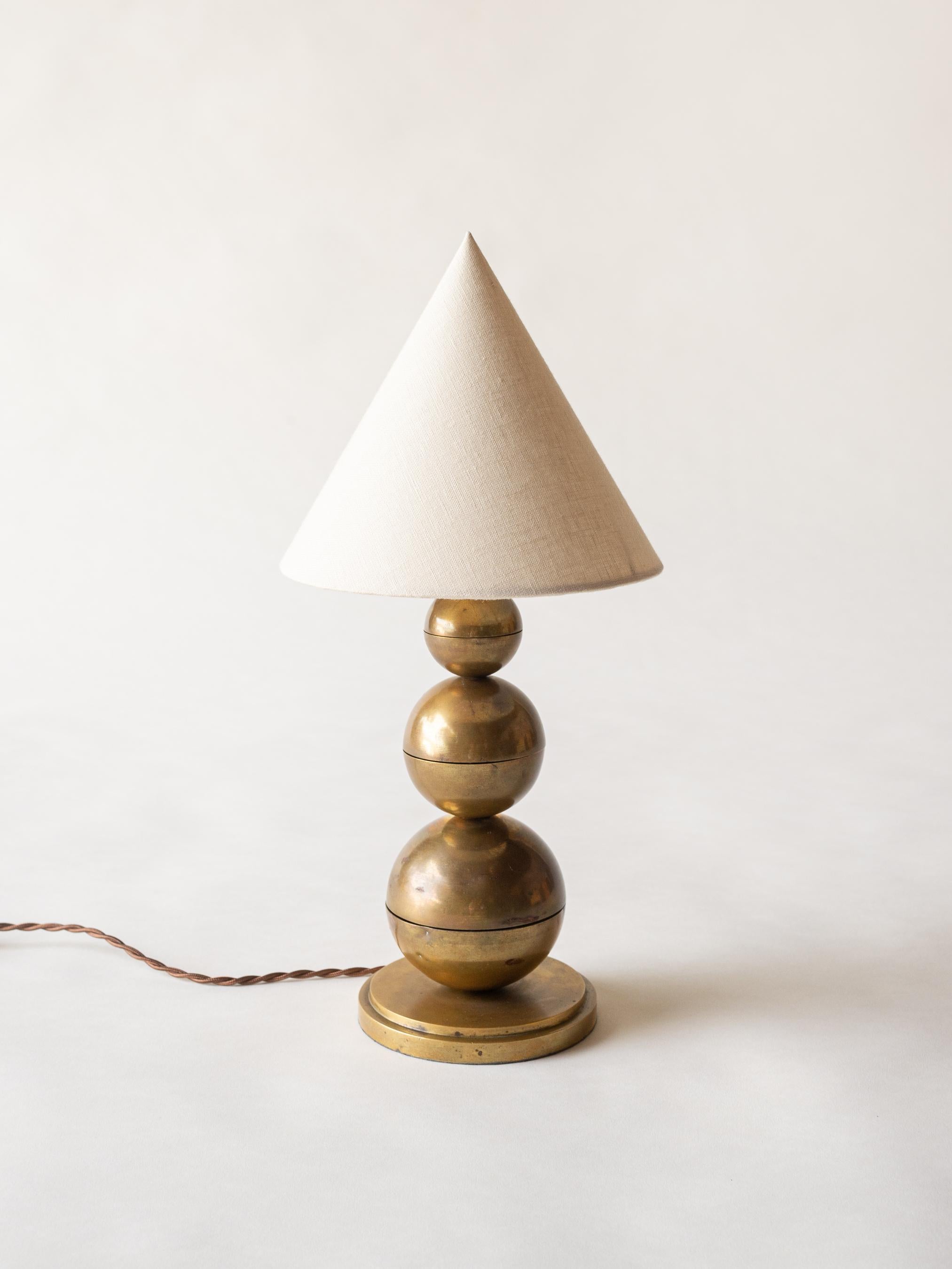 A eye-catching, structural table lamp by Jean Boris Lacroix (1902-1984). The lamp base is structured out of three brass spheres, stacked in graduating size from large to small with rich, original patina. Topped with a custom and period appropriate