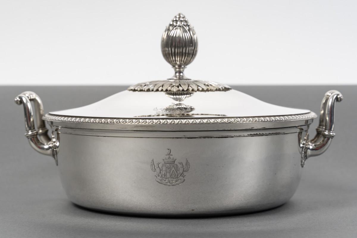 Gemüseschale aus Sterlingsilber. Der schlichte Korpus ist am Hals mit einer Borte eingefasst und wird auf beiden Seiten von Henkeln flankiert, die mit einer Halbmuschel verziert sind. Der Deckel ist mit einem Fries aus Palmetten umgeben, und der
