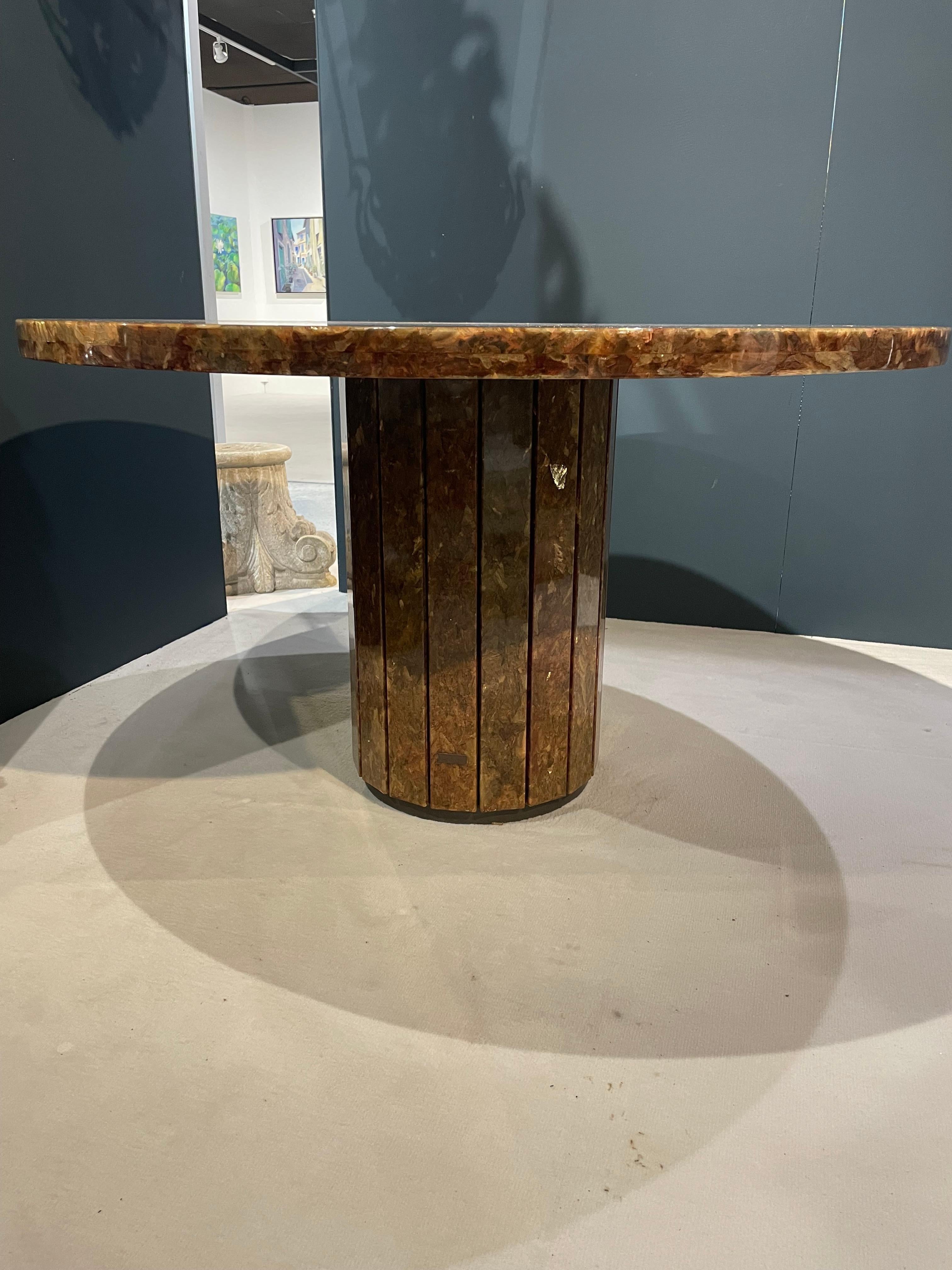 Jean CHARLES for Maison CHARLES. Large round table entirely covered with resin, on a wooden core, decorated with inclusions. The central foot, in faceted cylinder, rests on a tiered base and receives the top decorated with an inlay brass crossbar.