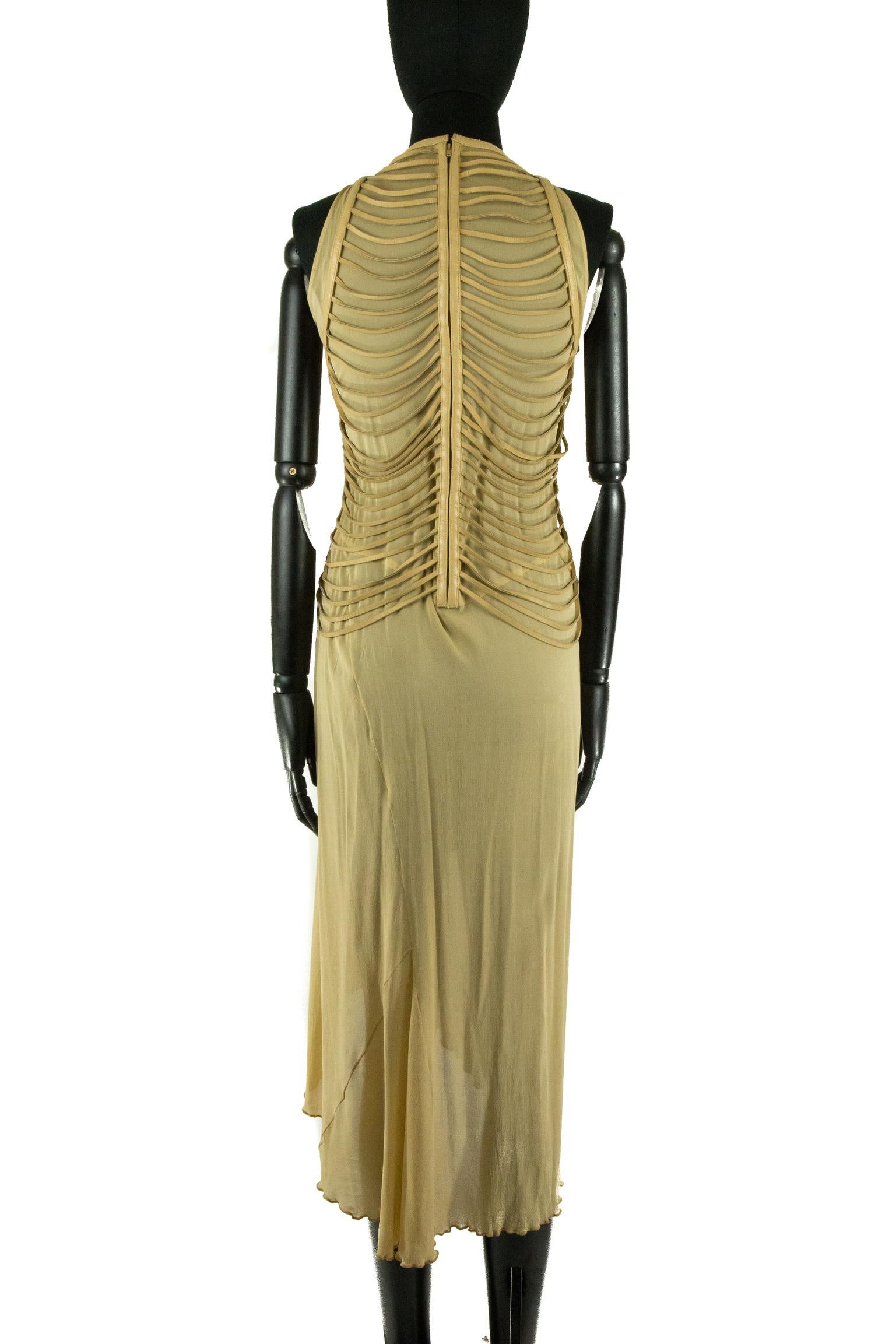 A Jean Claude Jitrois chiffon taupe maxi dress with a layer of beige leather fringing draped perpendicular across the bodice. The dress is sleeveless and features a curved wrap in the front. The dress is fastened down the centre back with a zip.
