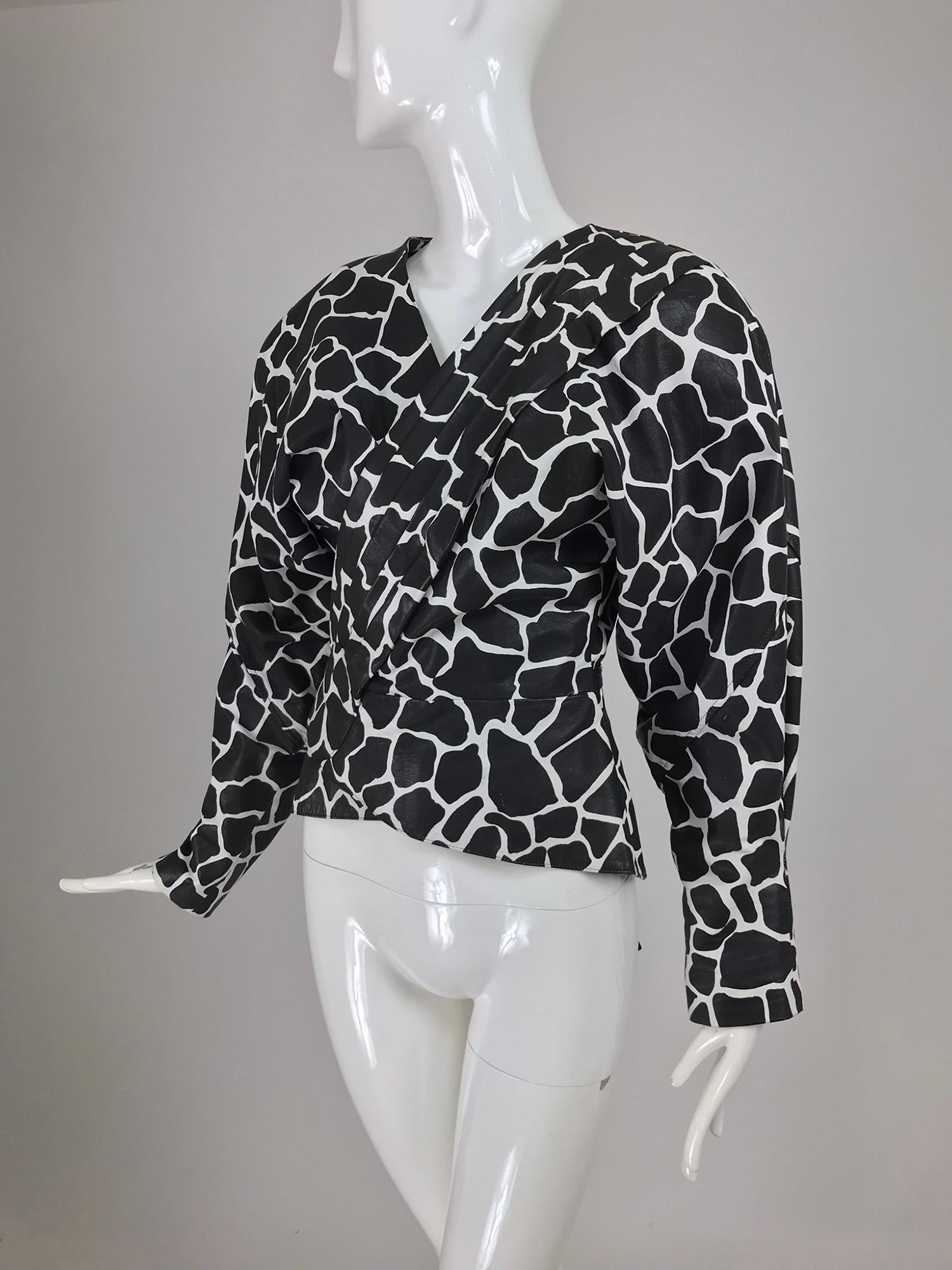Jean Claude Jitrois black and white leather wrap jacket from the 1980s. Black and white leather in an animal/giraffe print, the jacket wraps at the front and has ties at the waist, with a peplum below. Padded shoulder, dolman sleeves that narrow at