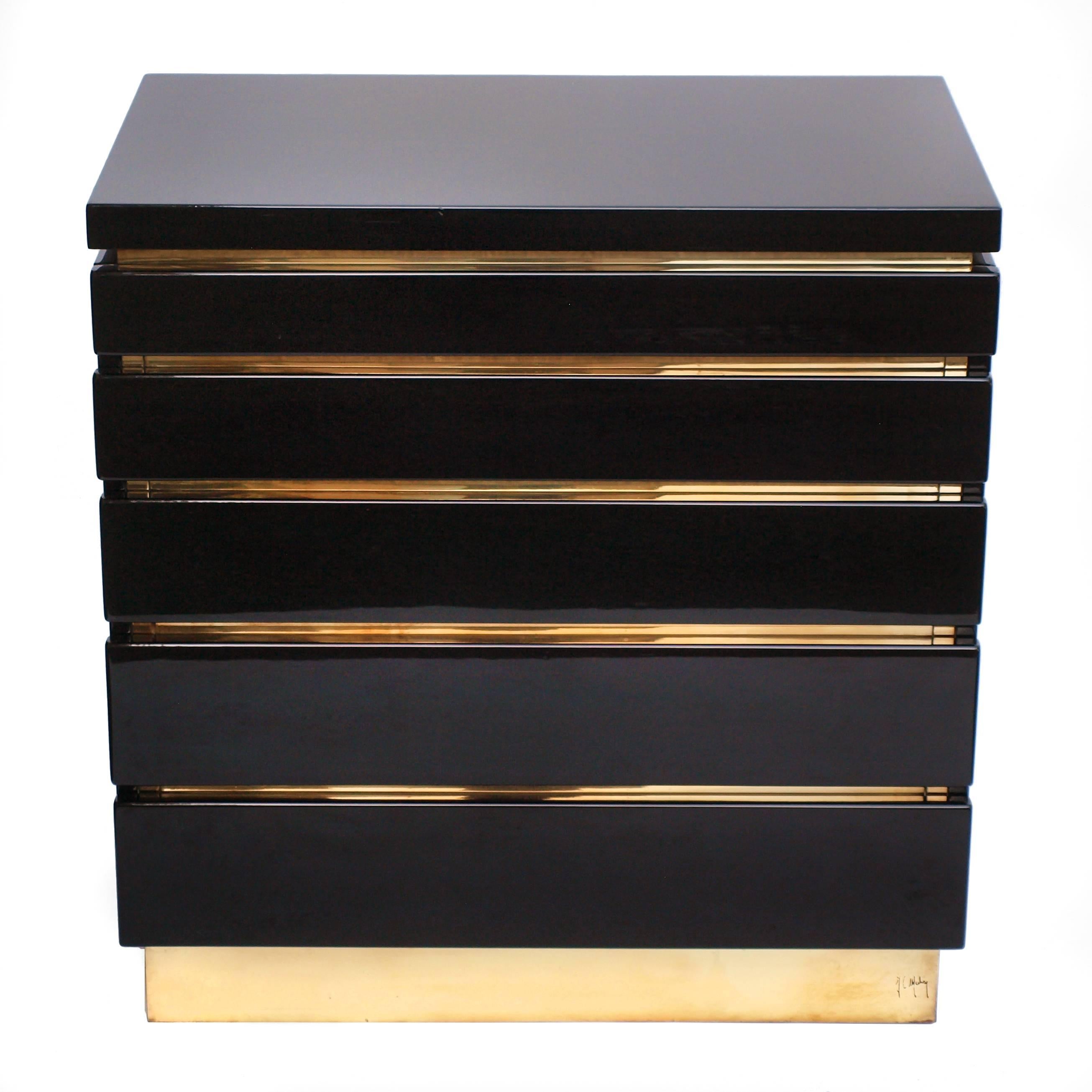 A 1970s sleek geometric chest of drawers by Jean Claude Mahey finished in a mirrored black lacquer with inset decorative brass edging sitting on a signed brass base. Five drawers descend to larger sizes and interior made from a blonde satinwood.
 