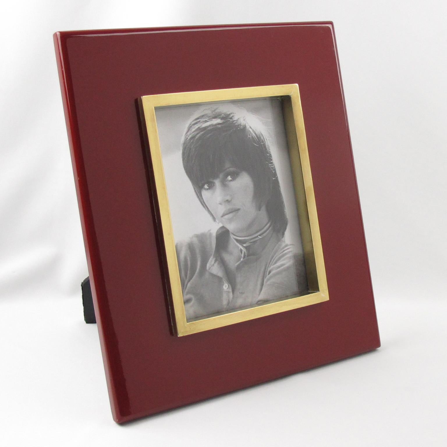 French designer Jean Claude Mahey designed and crafted this luxury modernist picture photo frame in the 1970s. The decorative piece features an elegant Oxblood colored lacquered wood with polished gilded brass framing around the picture view. The