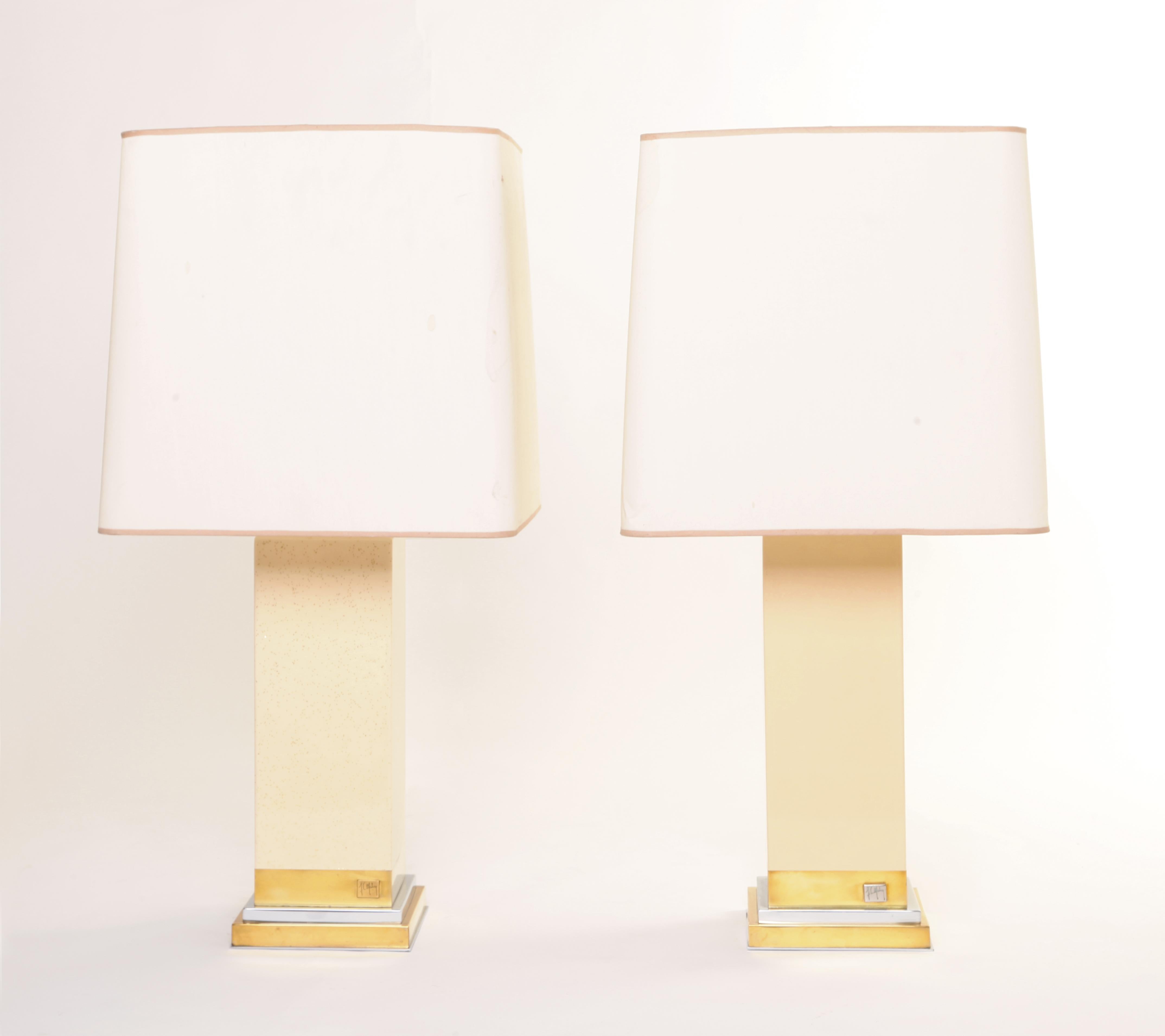 Une quasi-paire de lampes signées par Jean Claude Mahey. Les deux reposent sur un socle en laiton et chrome, et tandis que l'un est laqué en crème unie, l'autre est laqué en crème pailletée d'or. Les deux lampes sont accompagnées d'un abat-jour en