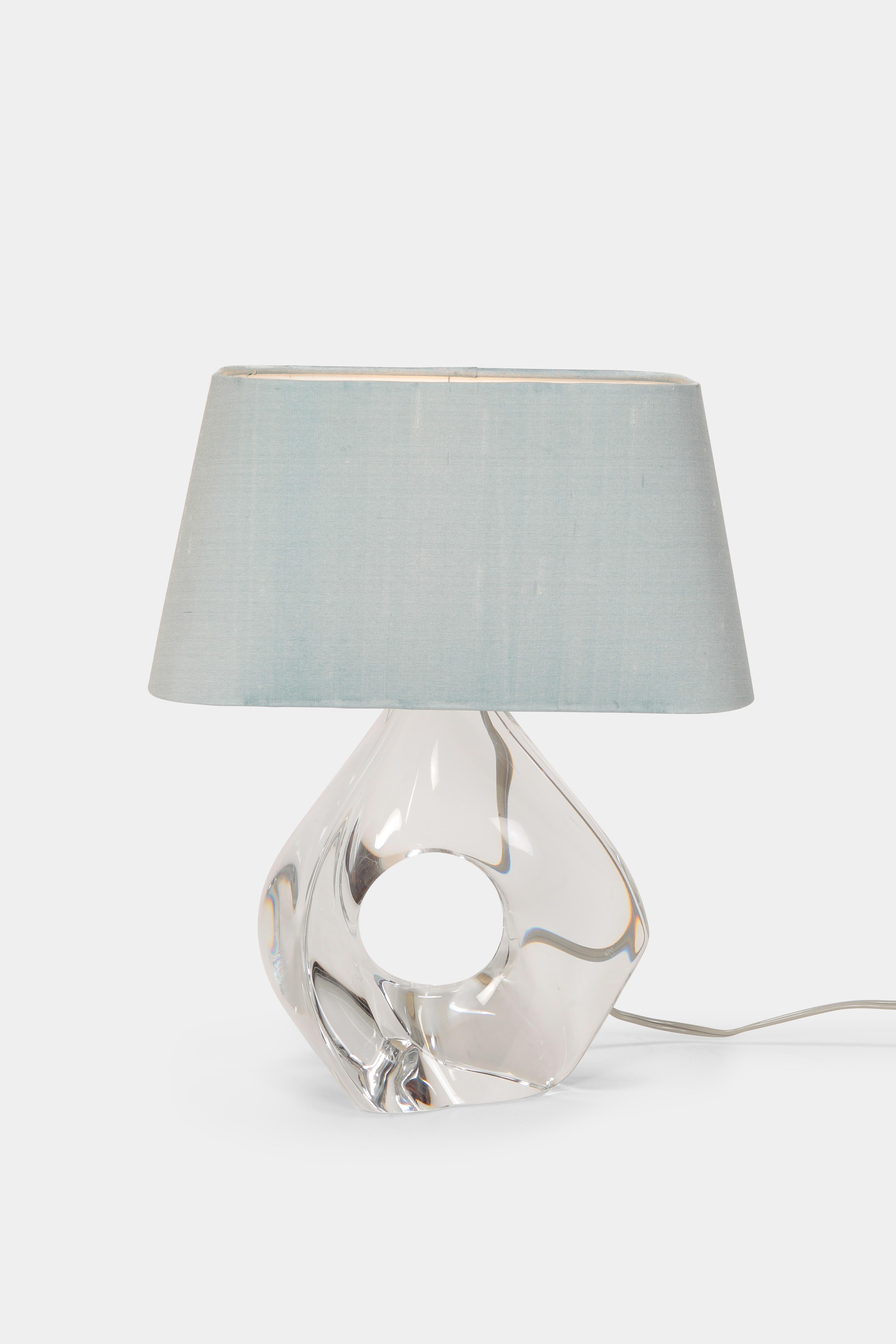 Jean Daum crystal table lamp manufactured by Daum France in the 1960s in France. Elegant shaped, sculptured base made of clear crystal glass. New ice blue cotton lamp shade. Graved from the manufacturer.