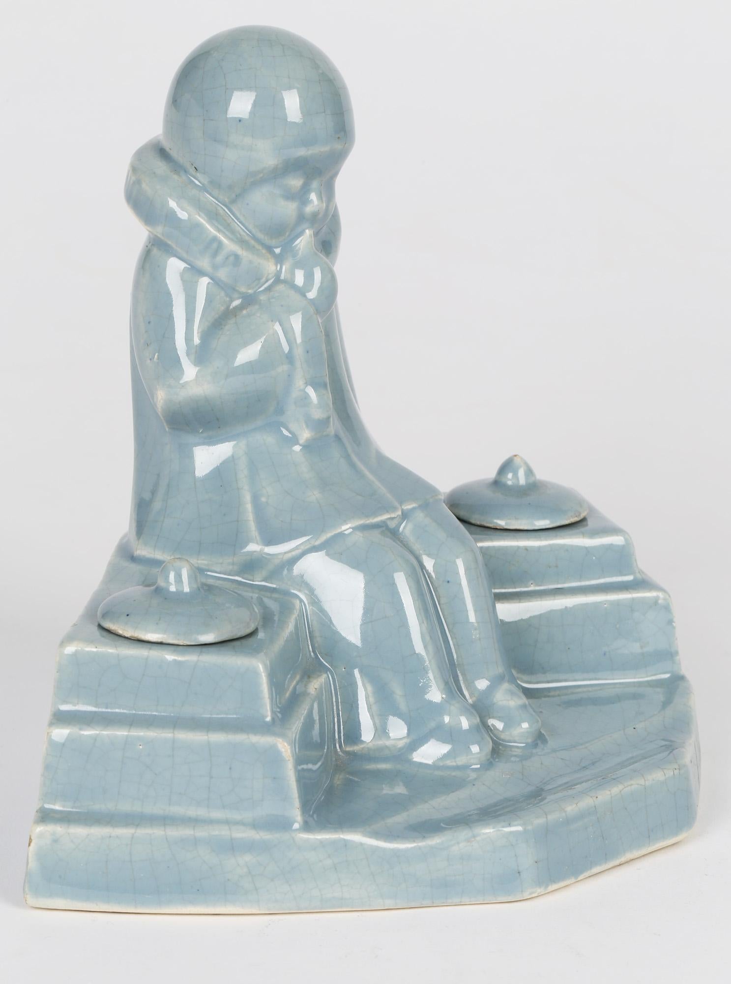 A stylish French Art Deco pottery inkstand with a seated child in a pierrot clown dress by Jean de la Fontinelle (1900-1974) and dating from around 1930. The pottery inkstand shows a young child in thought and sat on a wall with lidded inkwells to