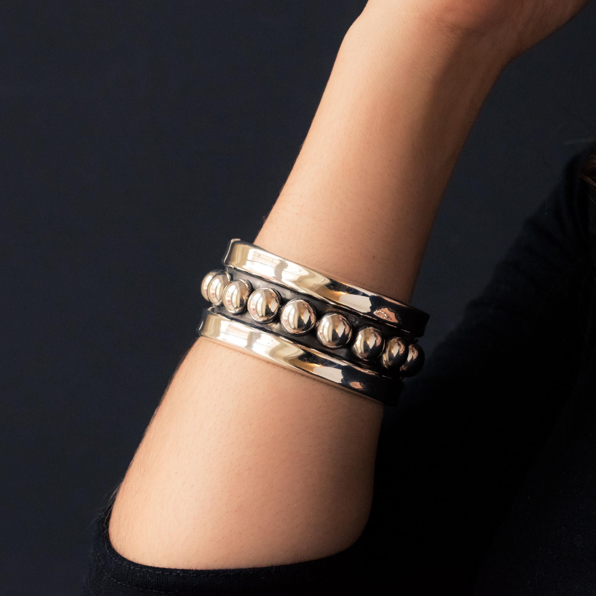 Bracelet in silver.
The large center of this silver bangle bracelet is adorned with silver pearls on a gray and matte background. On both sides, the edges form a slight gutter. It is opening on the top by a spring hinge located at the base.
Inner