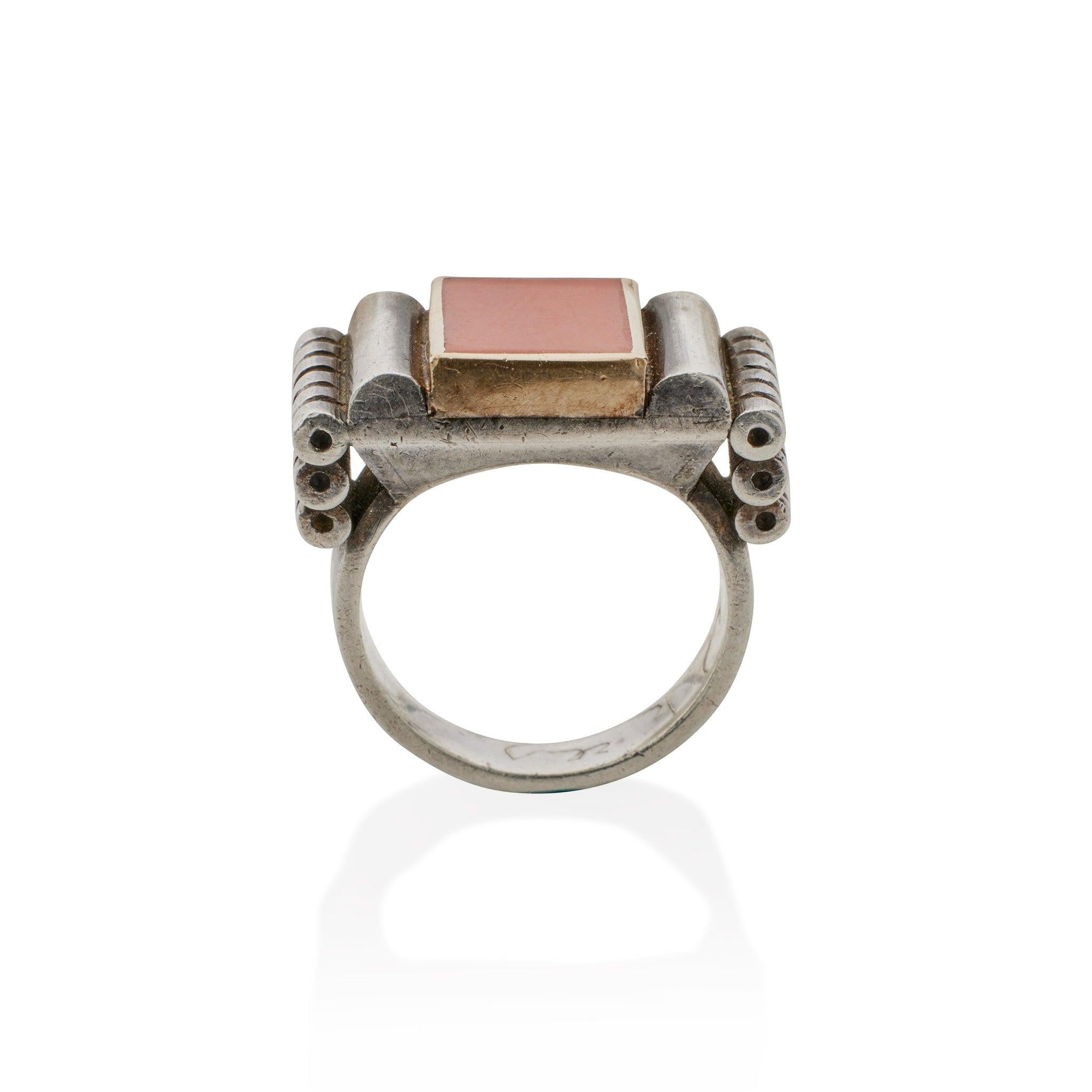 Designed and made by hand by Jean Després in the 1930s, this silver ring is set with a square coral within a gold surround flanked by silver rolls and tiers of descending ring turned cylinders. Beautifully engineered to balance lightly on the hand,