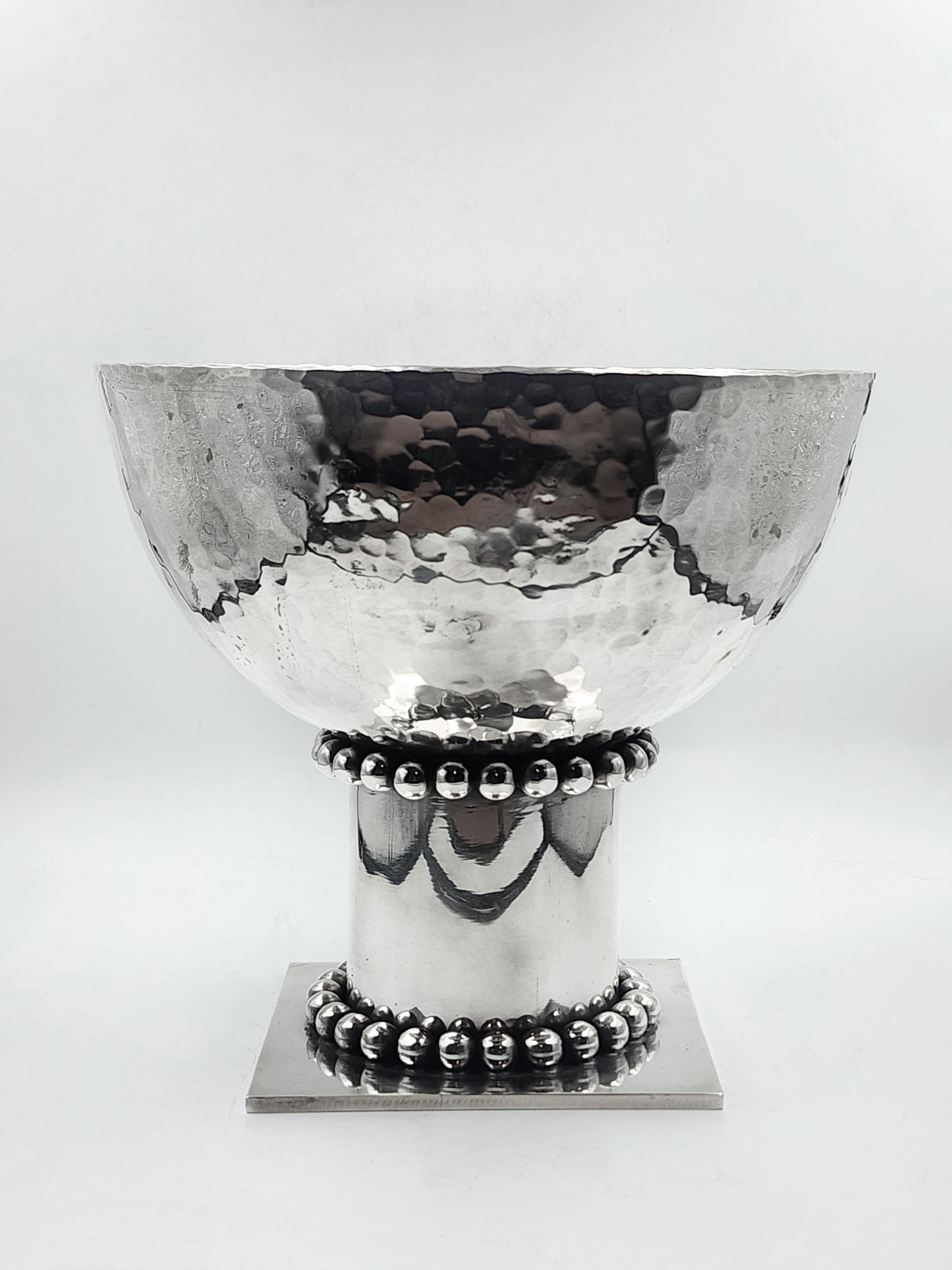 Centrotavola Art Deco in argento di Jean Despres
Questo centrotavola Art Deco di Jean Despres presenta un design distintivo con una forma a ciotola arrotondata e una base cilindrica. La ciotola è realizzata in metallo argentato con una texture